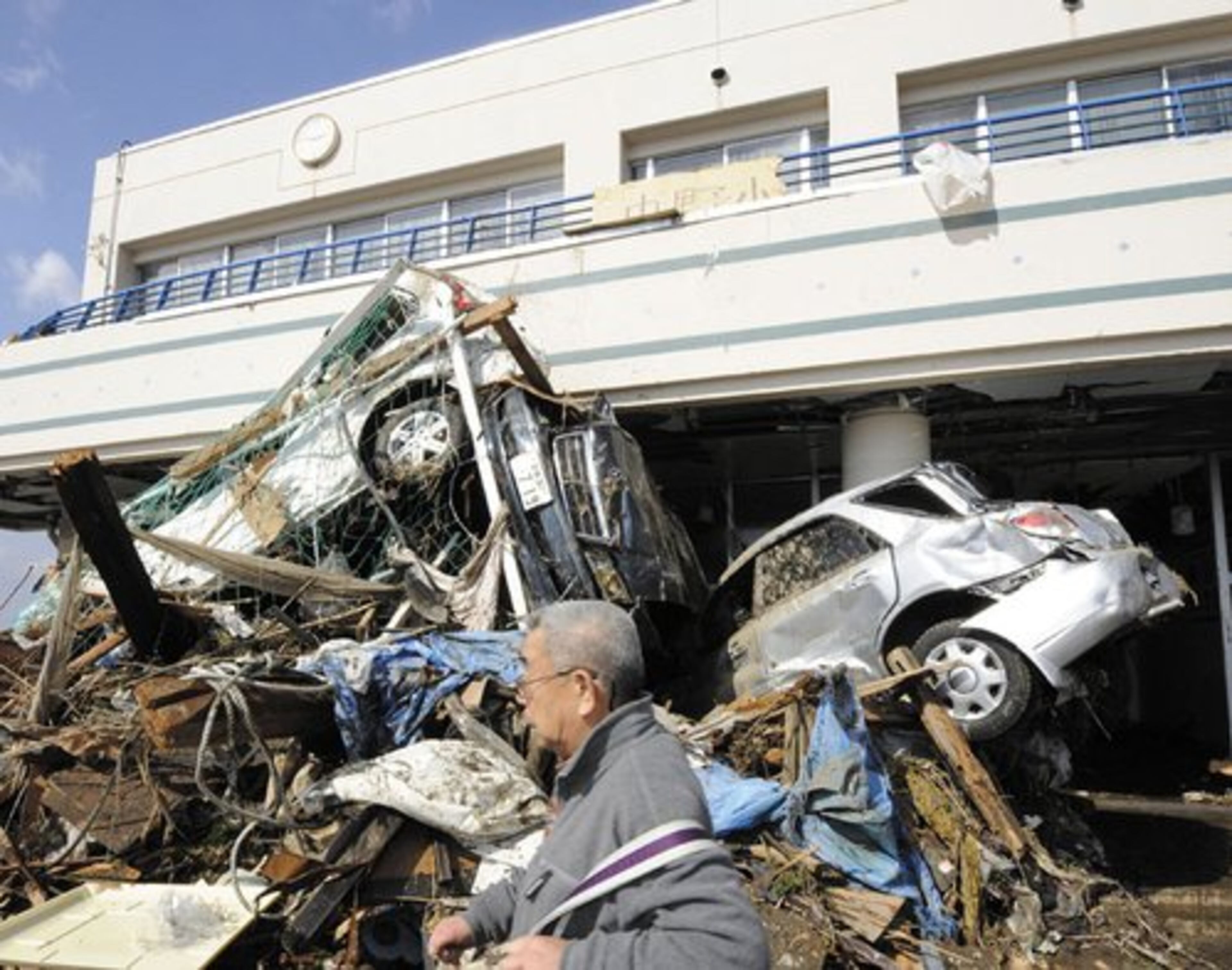 A man walks past vehicles which were washed away by tsunami into the entrance of an elementary school in Sendai, northern Japan.