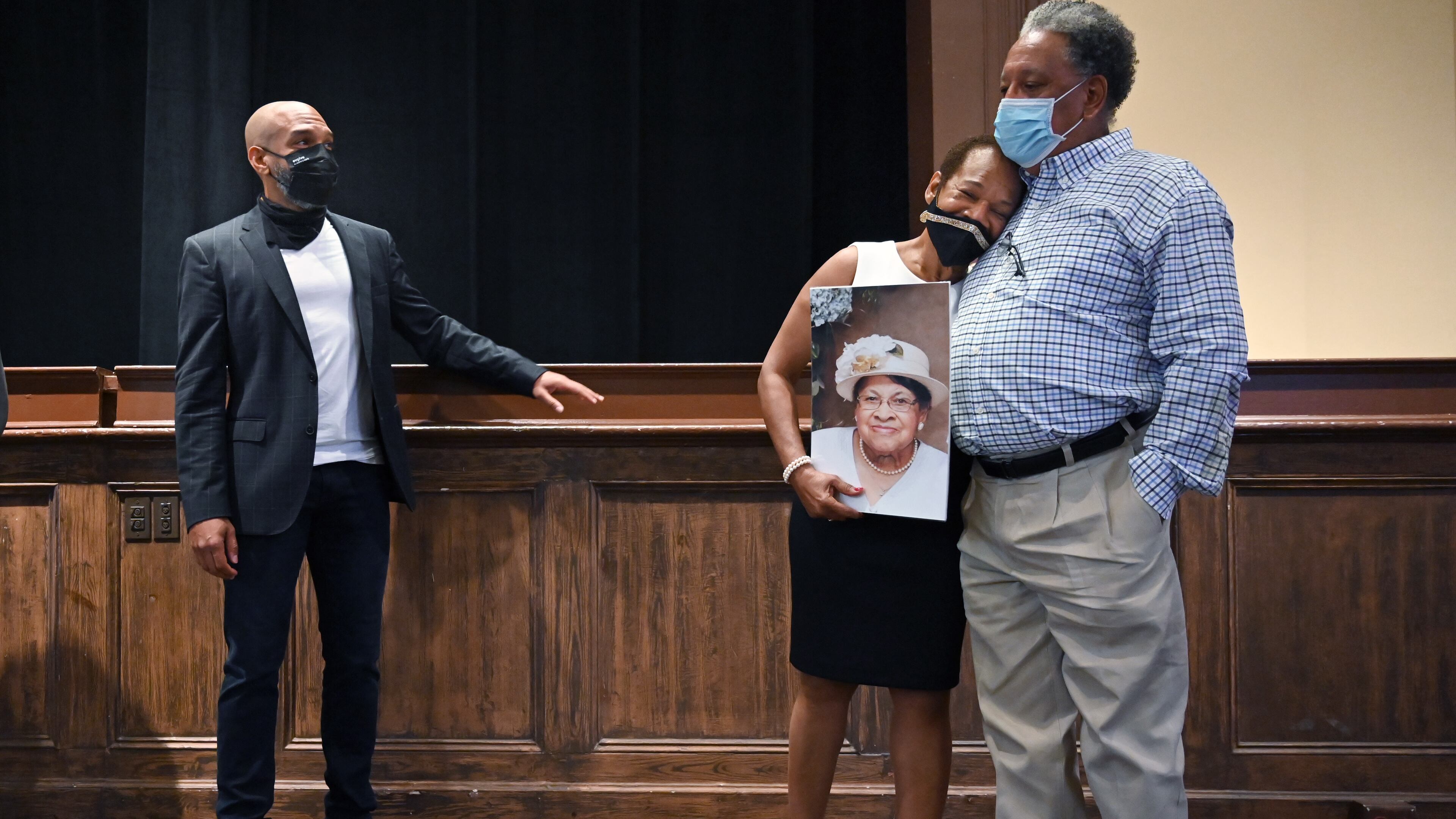 Gwendolyn Payton hugs her cousin Vernon Middleton as one of her children, "Walking Dead" actor Khary Payton (left), looks on during the artist talk for her new gallery exhibition, "The Faith of The Dreamer: Opposition to the Truth May Derail the Dream but the Faith of the Dreamer Prevails," at Plunkett Gallery in the Hardman Hall Fine Arts Building at Mercer University in Macon on Friday, Sept. 25, 2020. Gwendolyn Payton, after nearly 50 years, is getting her senior art show that was denied to her by the head of the Mercer art department at the time. She is holding a photo of her mother, Johnnie Mae Middleton, who died earlier this year. Hyosub Shin / Hyosub.Shin@ajc.com