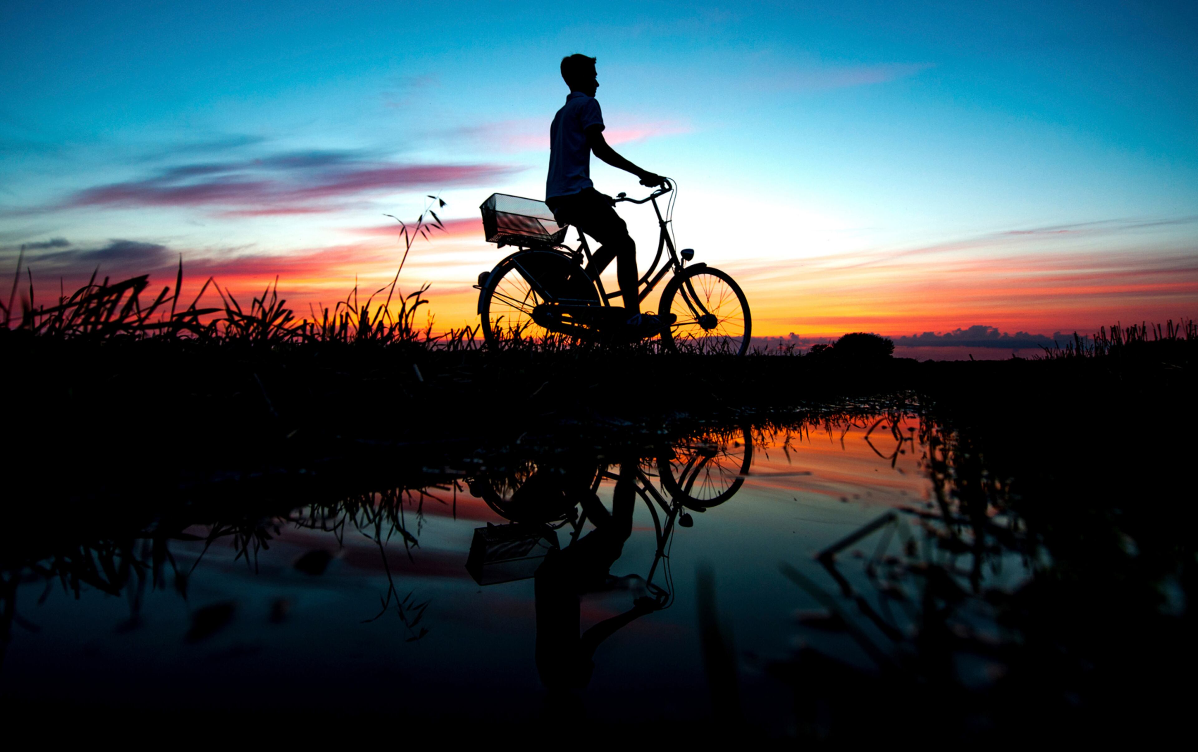 In this photo taken Monday, July 31, 2017 a young man cycling along a path is silhouetted against the sunset in Oldenburg, Germany. (Hauke-Christian Dittrich/dpa via AP)