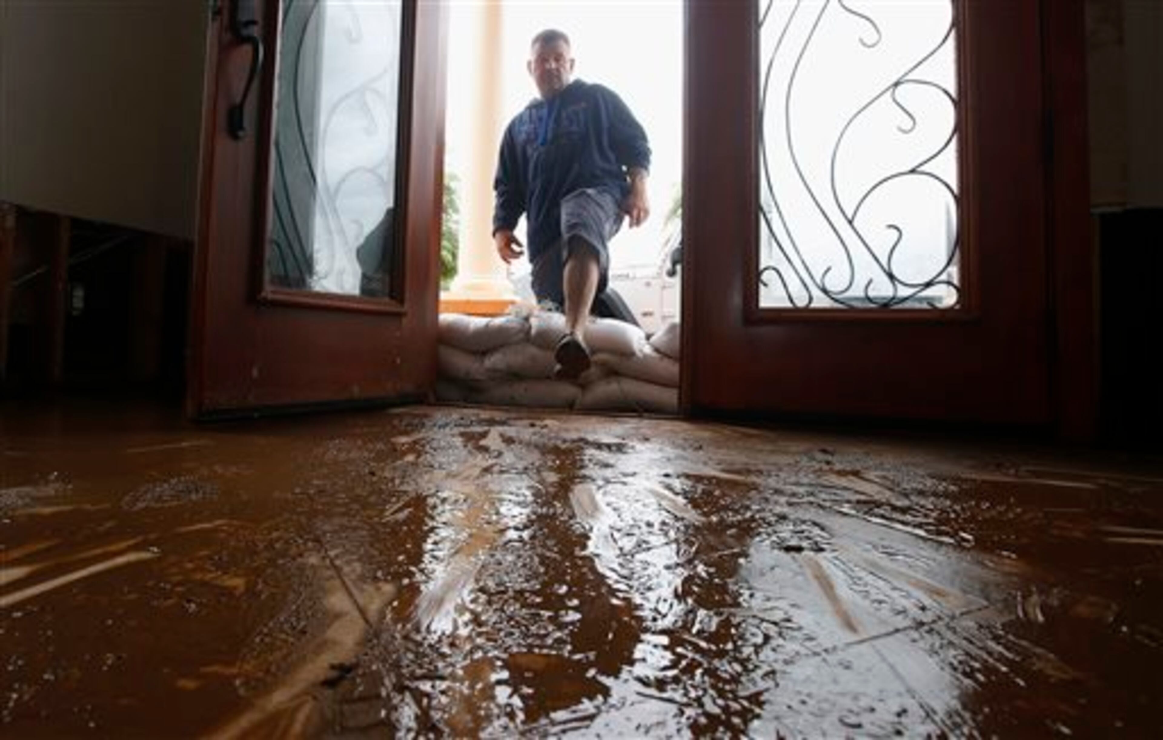 Nick Kriaris steps over sandbags as he enters his home onto mud-covered floors after his home flooded after heavy rains rolled through the Phoenix area Monday, Sept. 8, 2014. Storms that flooded several Phoenix-area freeways and numerous local streets during the Monday morning commute set an all-time record for rainfall in Phoenix in a single day. (AP Photo/Ross D. Franklin)