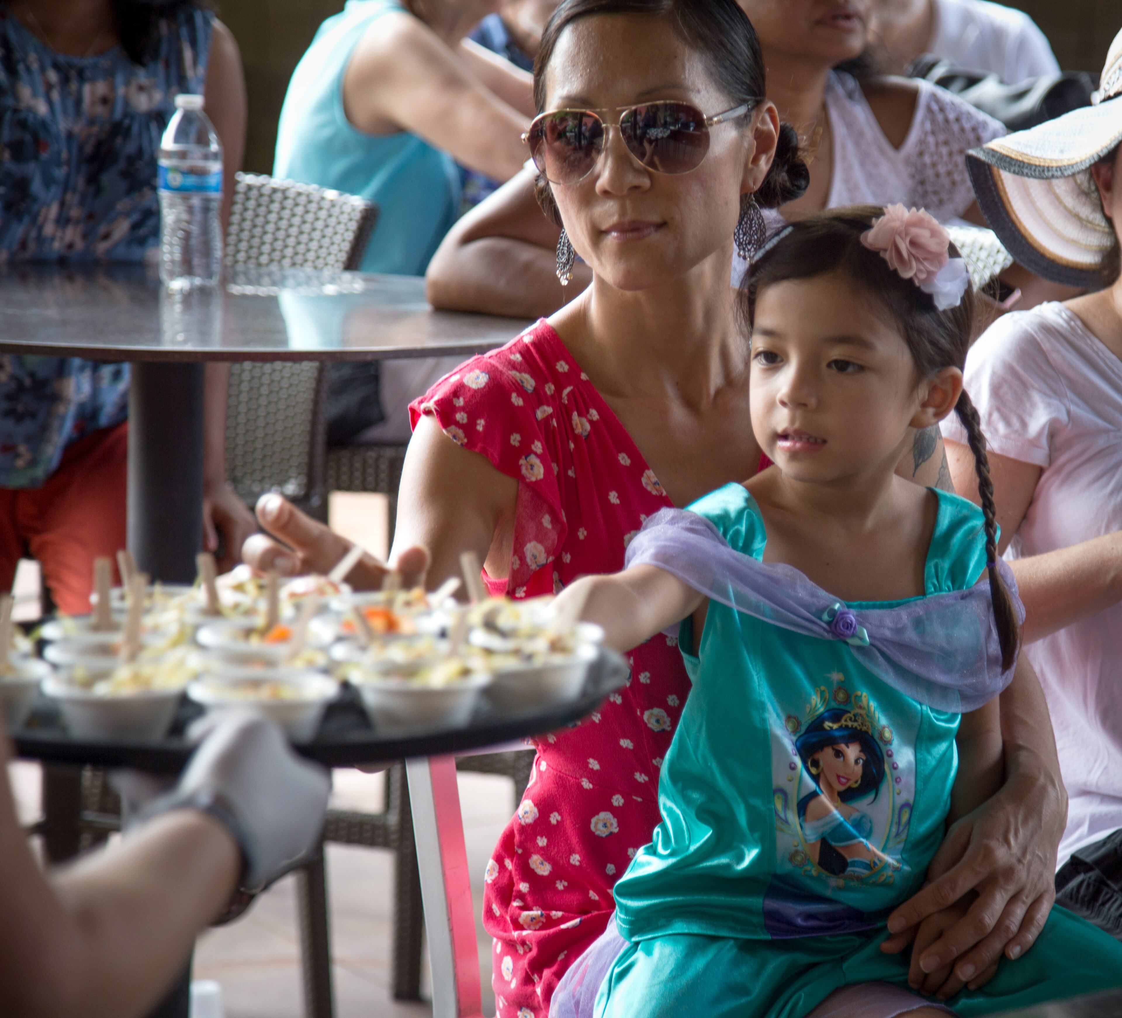Mila Konomos and her daughter Magenta,4, reach for a sample of the Fermented Tea Salad made by Clarkston High School students during the Refugee Recipe Celebration at the Atlanta Botanical Garden Sunday, June 24, 2018. STEVE SCHAEFER / SPECIAL TO THE AJC