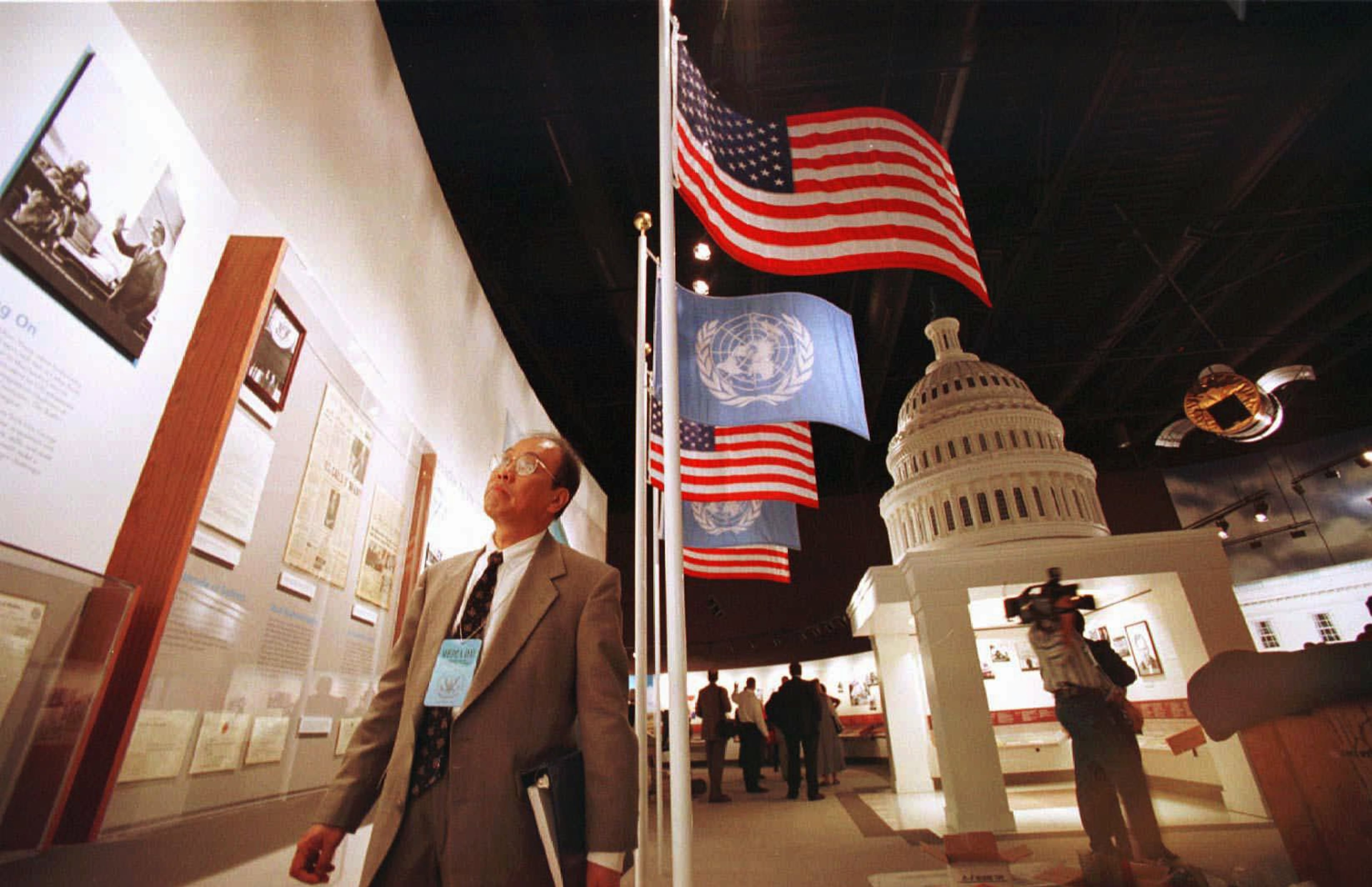 A visitor looks over the exhibits in the George Bush Presidential Library and Museum in 1997, prior to the formal dedication on the campus of Texas A&M University in College Station, Texas. The visitor is looking at the United Nations Ambassador section of former President Bush's career. In background is a replica of the U.S. Capitol building, which represents Bush's career in the U.S. Senate. At center are American and United Nations flags.