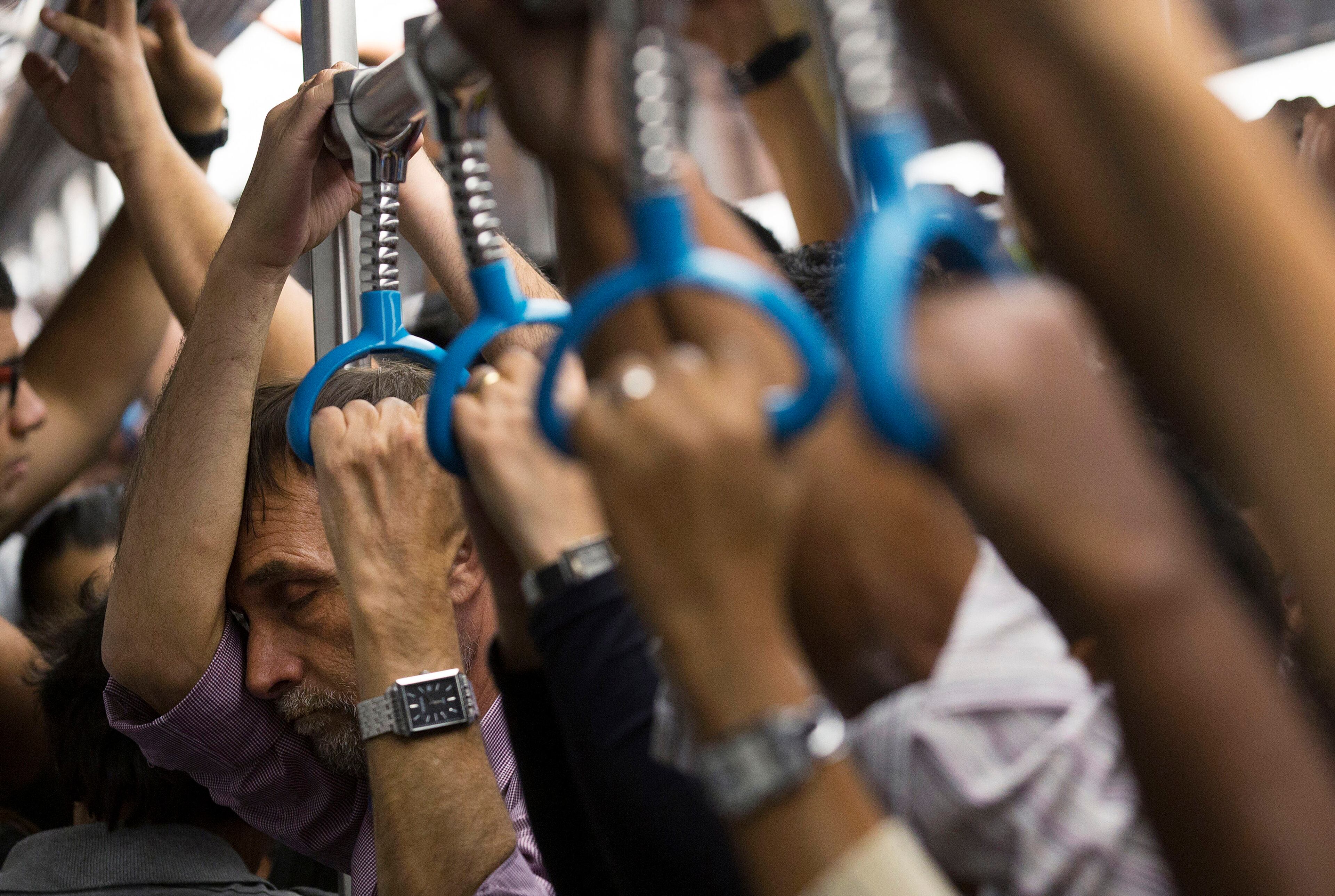 In this Sept. 17, 2014, photo, a man closes his eyes as he stands with other commuters in a crowded metro car during rush hour in Rio de Janeiro. On packed subways and crowded highways, billions of people worldwide participate in the daily commute to and from work. (AP Photo/Leo Correa)