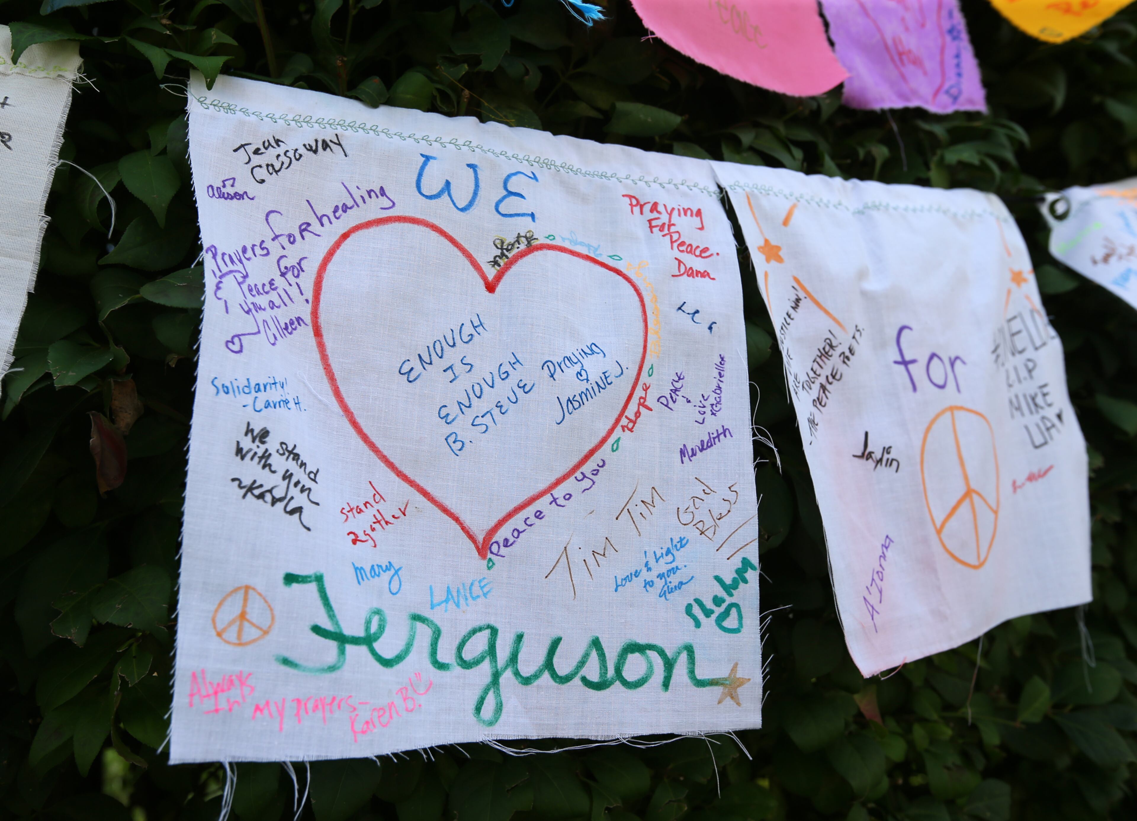 082114 Ferguson: A cloth sign hangs on a bush near the shrine for Michael Brown where he was shot and killed in the Canfield Apartments on Thursday, August 21, 2014, in Ferguson. CURTIS COMPTON / CCOMPTON@AJC.COM