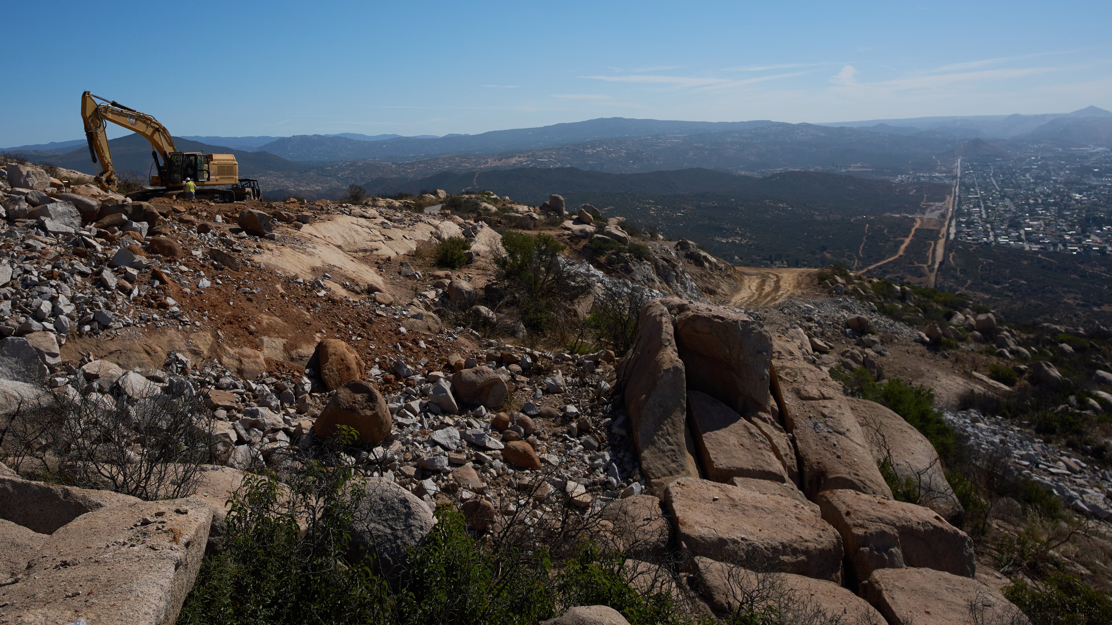 Construction crews work on a new border wall segment on Kuuchamaa Mountain, Friday, April 24, 2026, seen from Tecate, Mexico. (AP Photo/Gregory Bull)