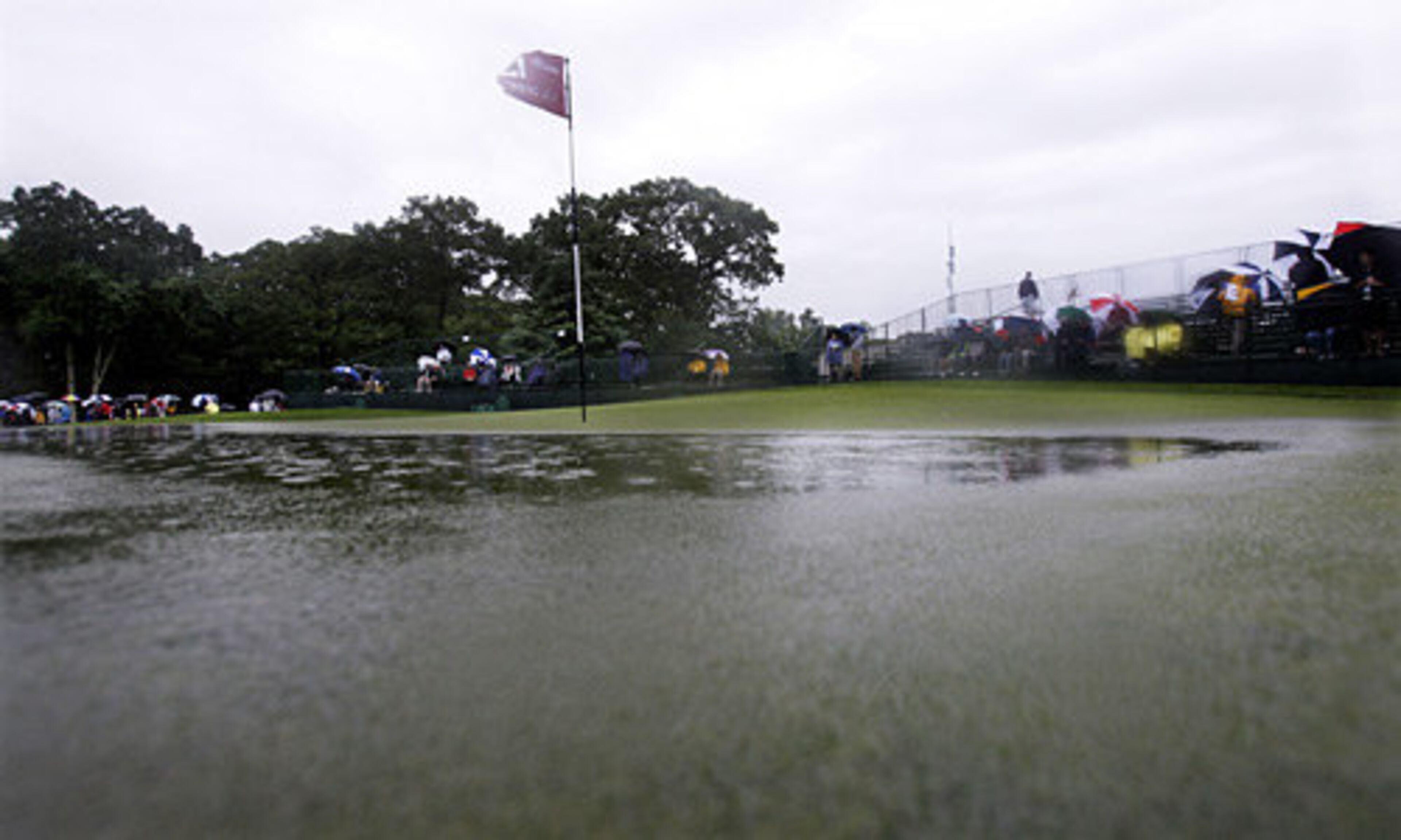 Water accumulates on the 13th green as spectators leave following suspended play because of heavy rain.