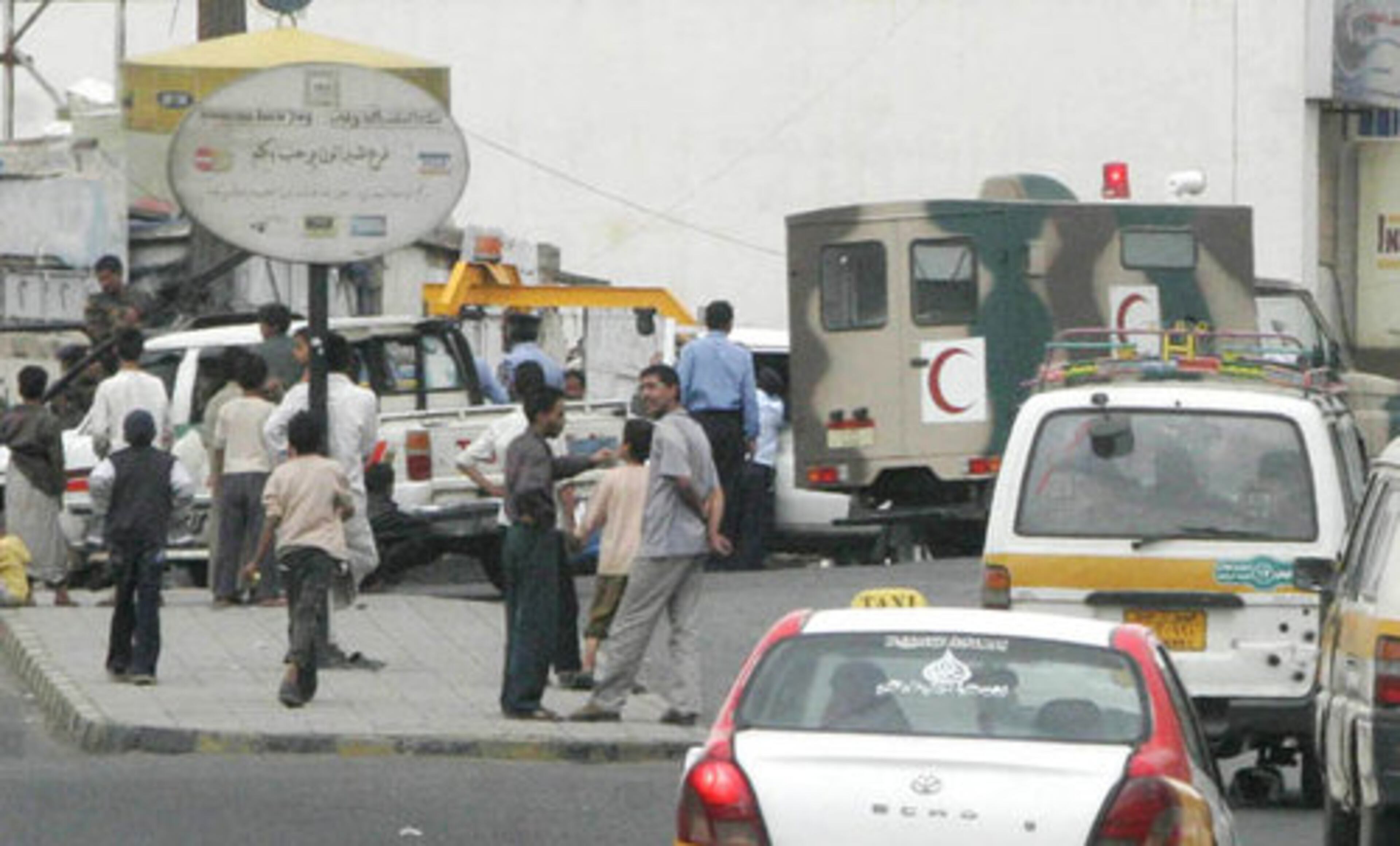 Yemenis talk as an army ambulalnce vehicle heads to the embassy.