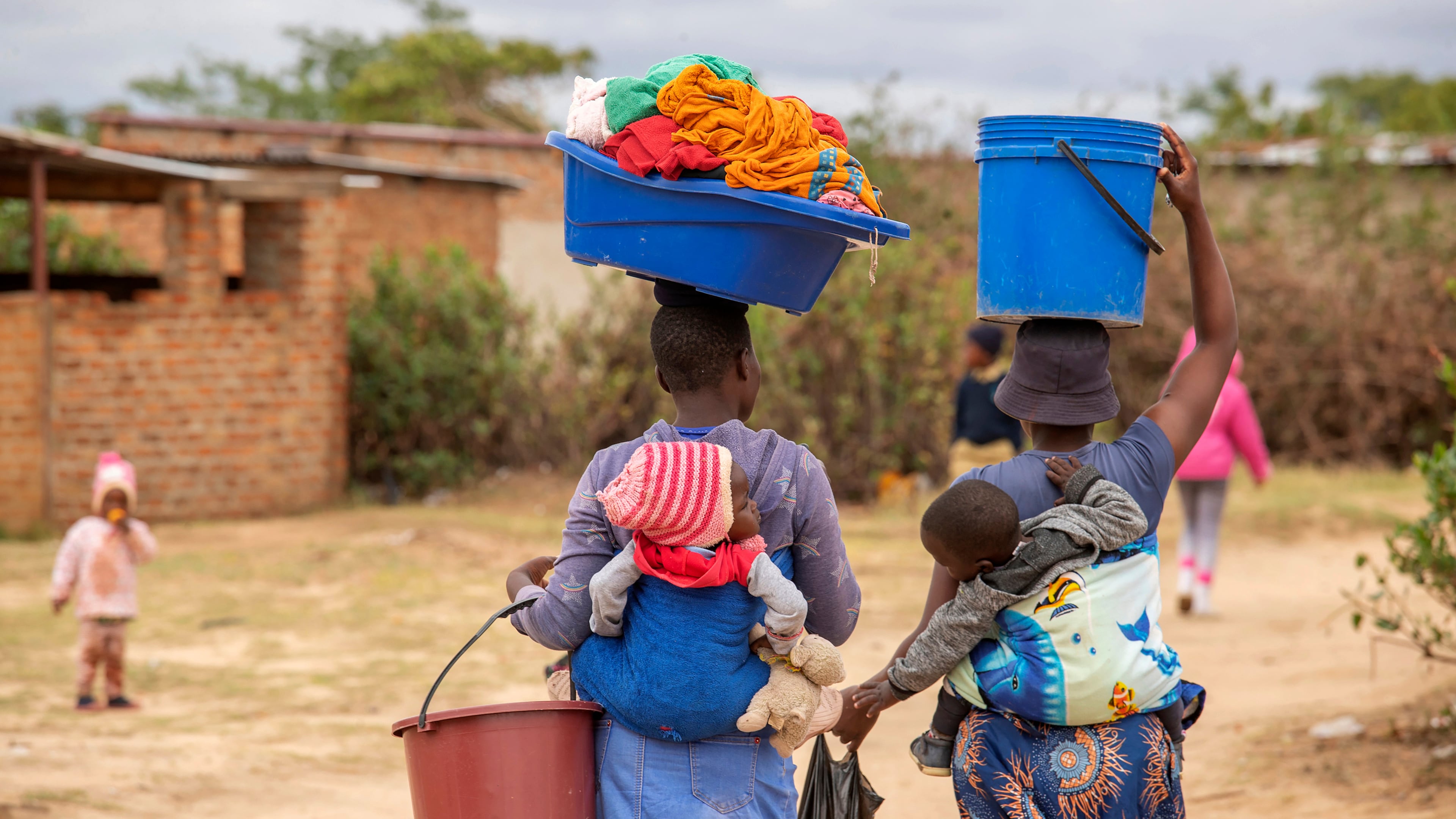 FILE - Women, with children on their backs, carry out chores in Epworth, Zimbabwe, on Nov. 14, 2024. (AP Photo/Aaron Ufumeli, File)