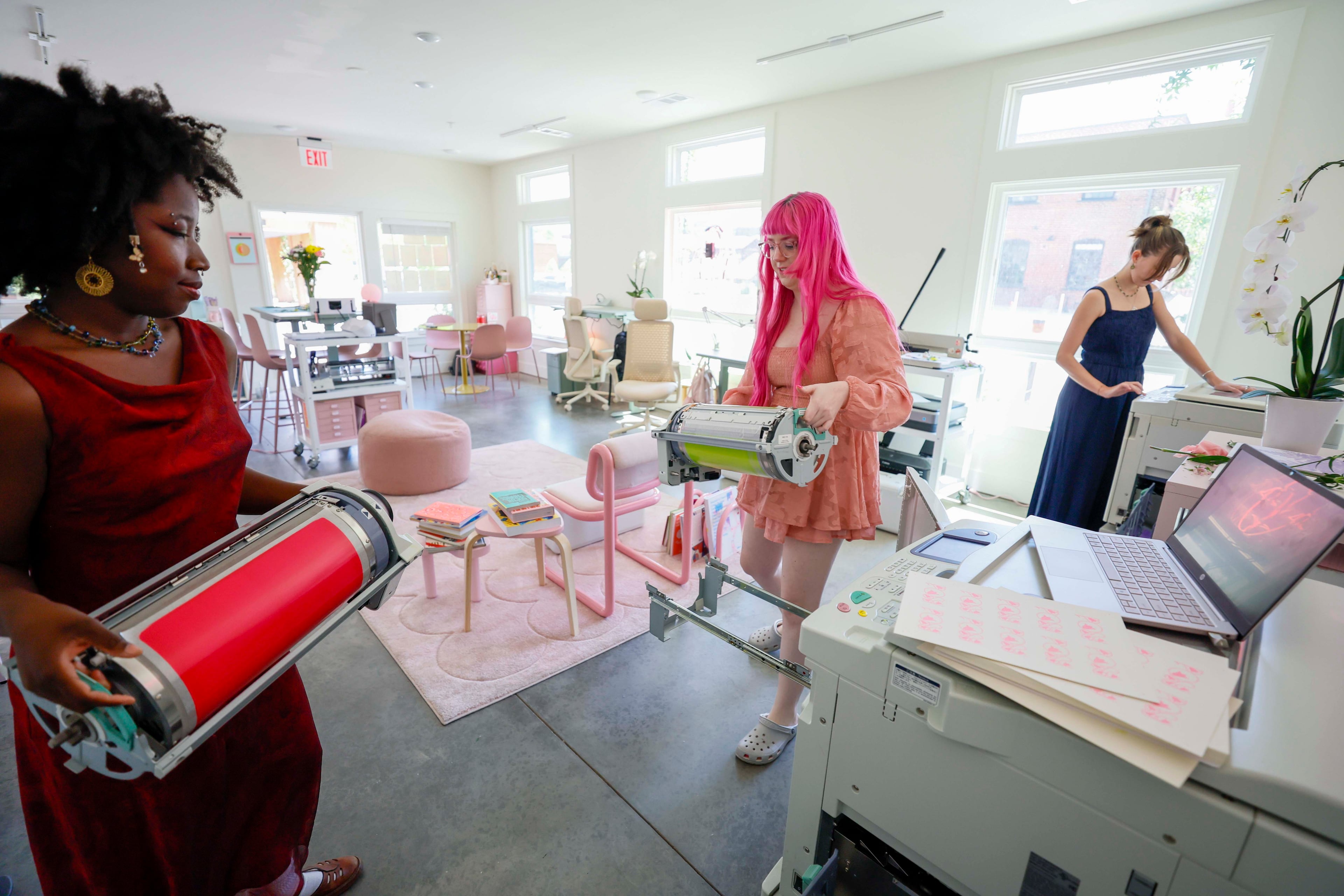 Workshop instructor Arantza Peña Popo (left) and studio founder Samantha Richardson (center) change Risograph machine ink drums at Posy Press while studio assistant Maddy Lyons works on a Riso print on another machine. (Miguel Martinez/AJC)