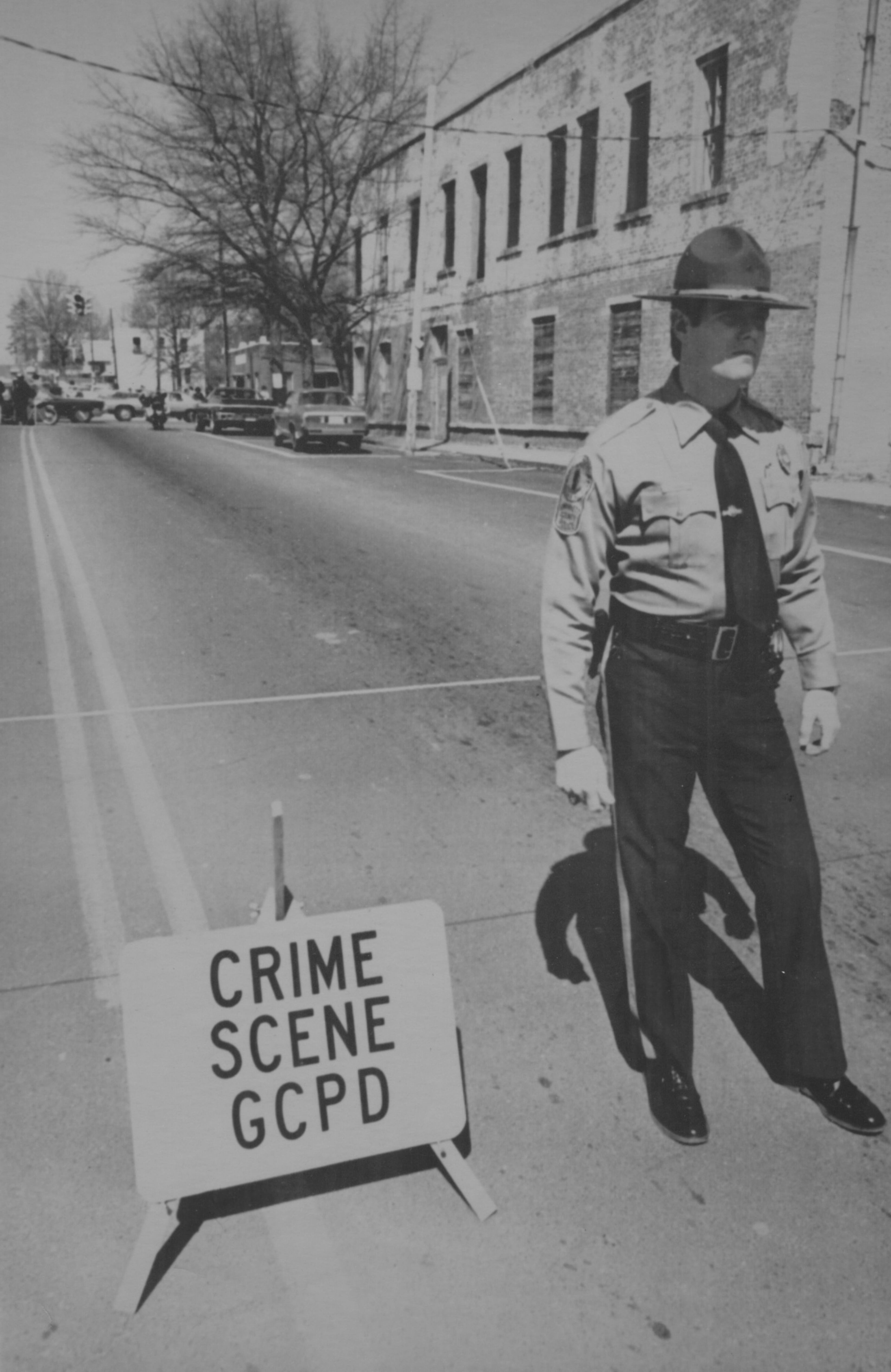 March 6, 1978 -- A Gwinnett County policeman stands guard at the scene in Lawrenceville where Larry Flynt, on trial for distributing the Hustler magazine he created, was critically wounded. Neil Shister, an eyewitness to the shooting, told reporters that he was following Flynt down the street when he "heard a loud report and looked to see if a car had backfired. I looked over at Larry and he was holding his stomach and sort of crumpling over." Shister, then freelancing for Flynt's Atlanta Gazette newspaper, ran to the sheriff's office for help. He said that he did not see who fired the shots at Flynt and Reeves.