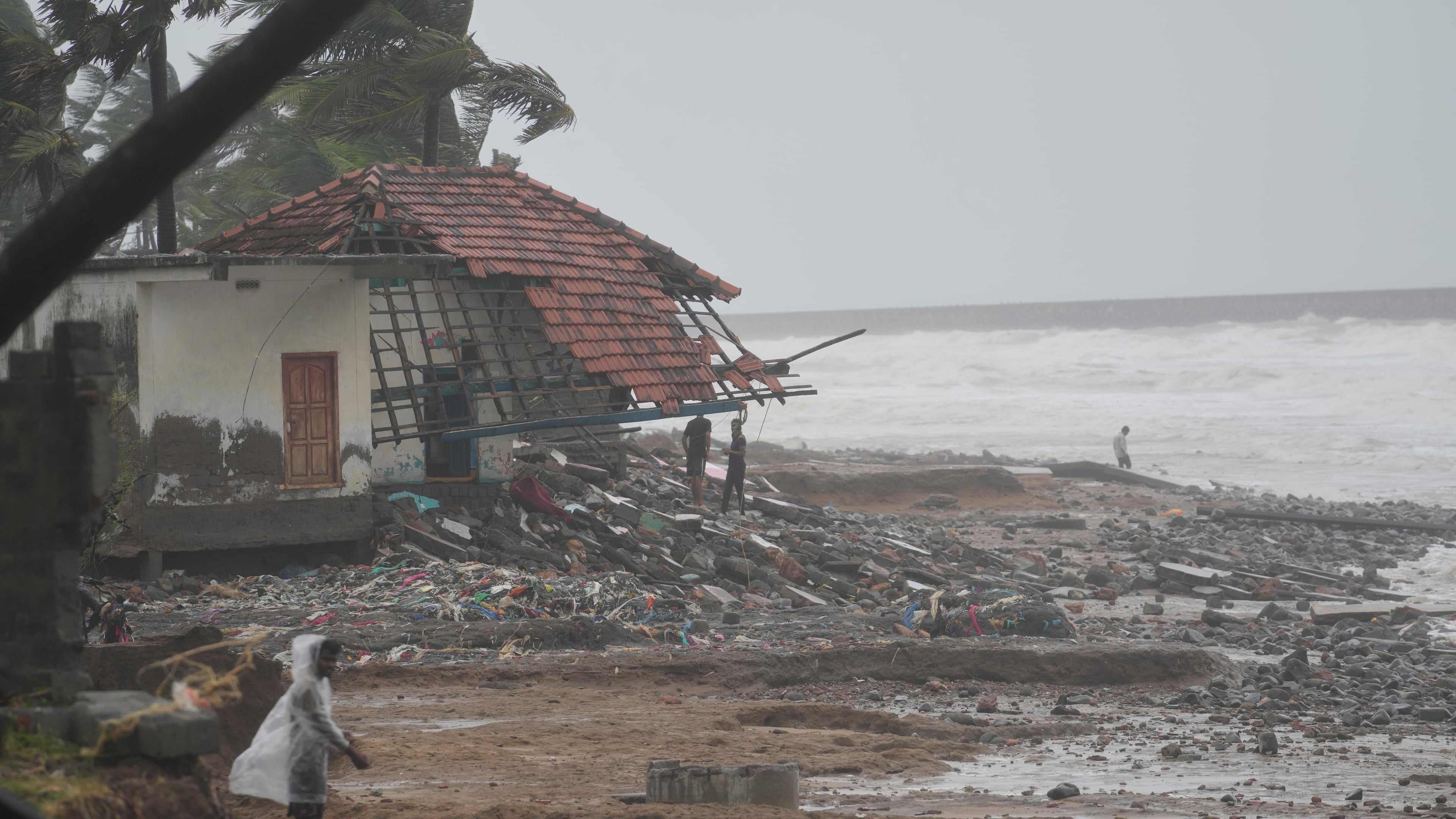 People walk past damaged homes near the shore at Uppada, in Kakinada, India, Wednesday, Oct. 28, 2026 after Cyclone Arnab crossed the Andhra Pradesh coast. (AP Photo/Mahesh Kumar A.)