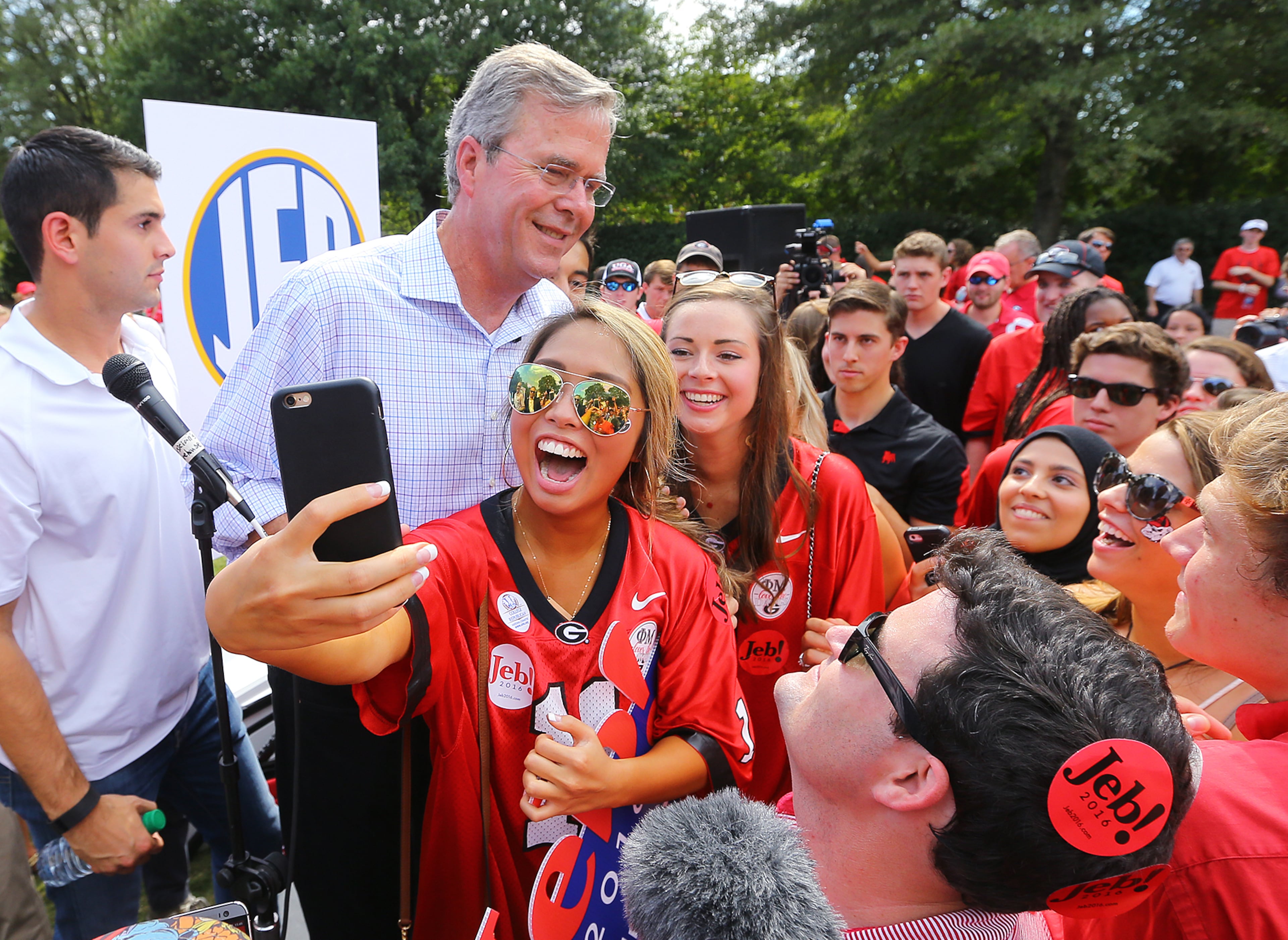 A UGA student snaps a selfie with GOP presidential candidate Jeb Bush (center left) while he works the crowd of 2015 University of Georgia game in Athens. (AJC 2015)