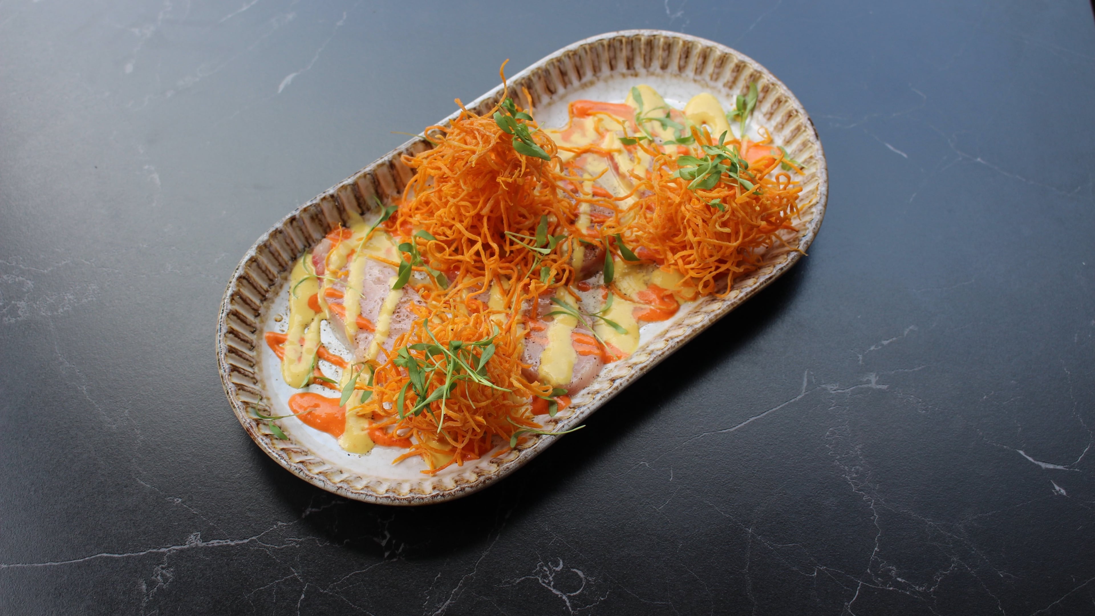 Hamachi tiradito has been on the menu of Fogon and Lions since they opened. Thinly sliced hamachi is arranged on sauces made from aji rojo and aji amarillo peppers and topped with fried sweet potato threads. (Courtesy of Fogon and Lions)