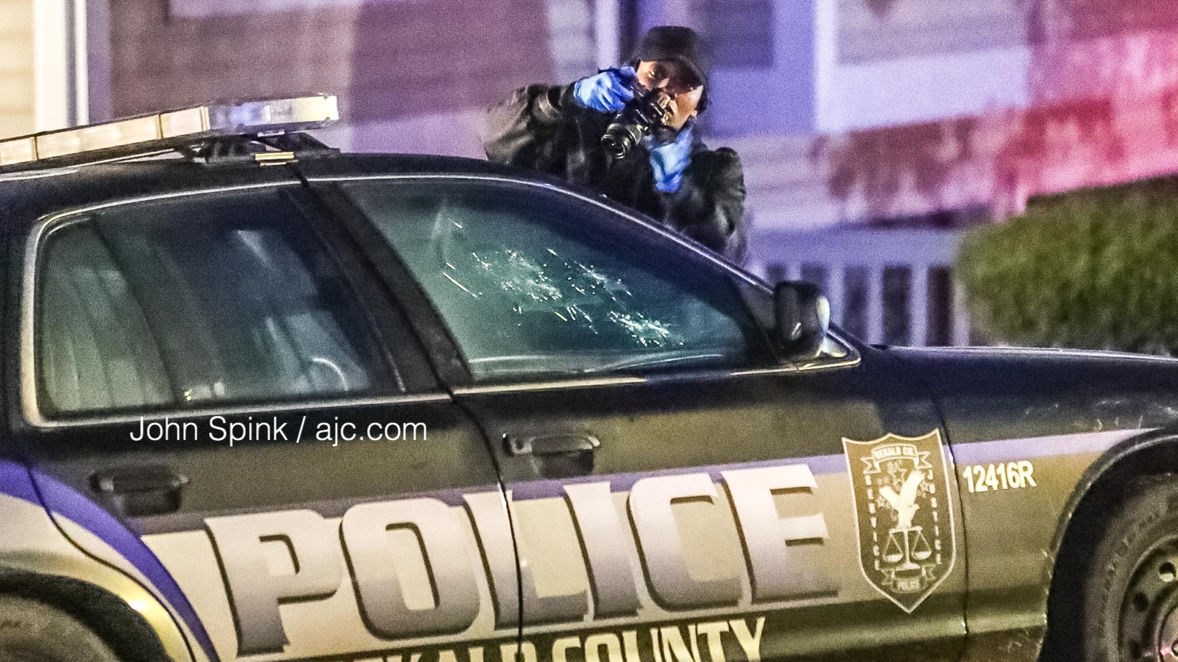 A DeKalb County police crime scene technician takes pictures of bullet holes in the front windshield of a cruiser on Raintree Bend.