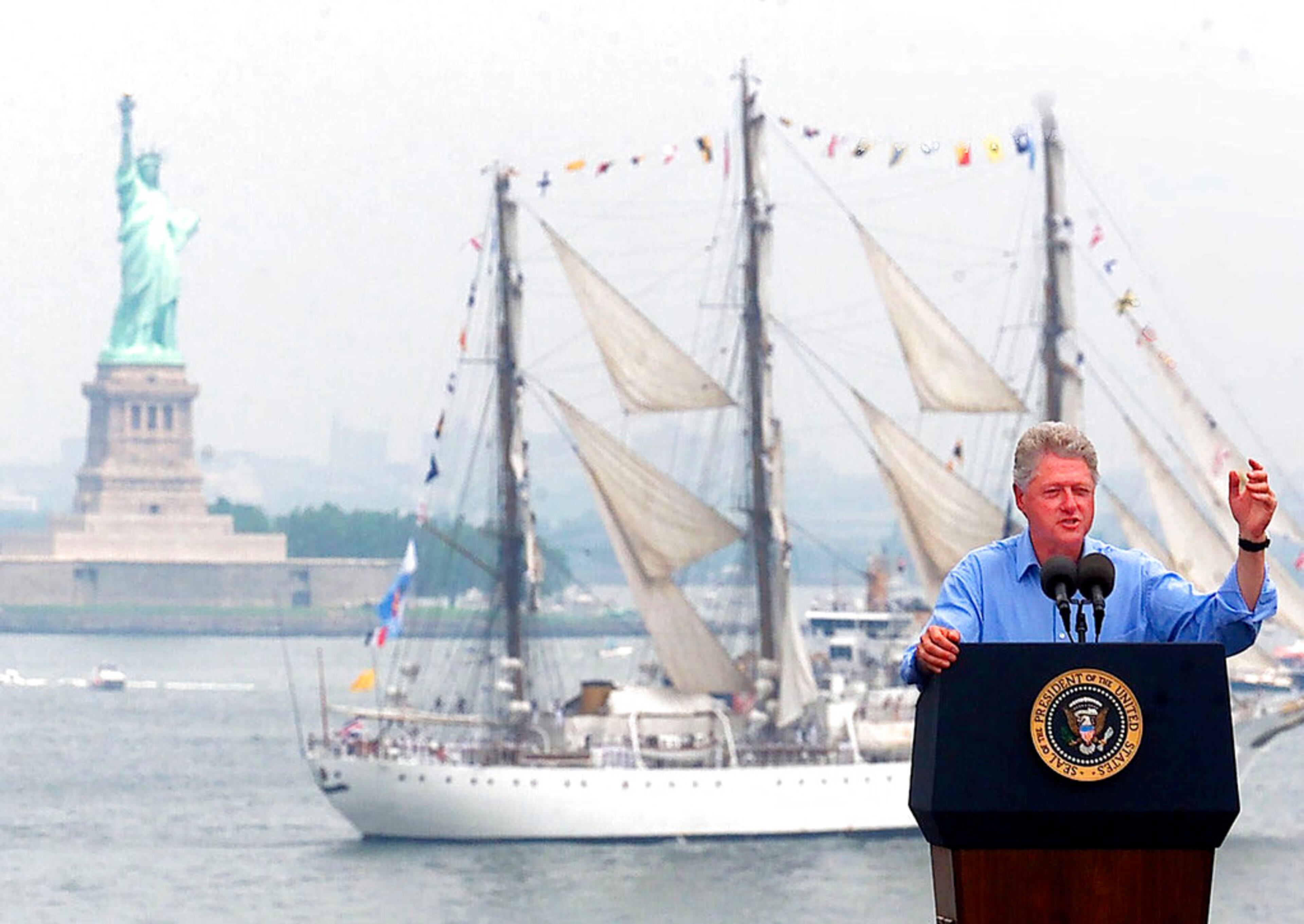 FILE - In this July 4, 2000 file photo, President Clinton speaks on the USS John F. Kennedy as a tall ship passes between him and the Statue of Liberty in New York Harbor during Independence Day celebrations in New York. (AP Photo/Ed Betz)