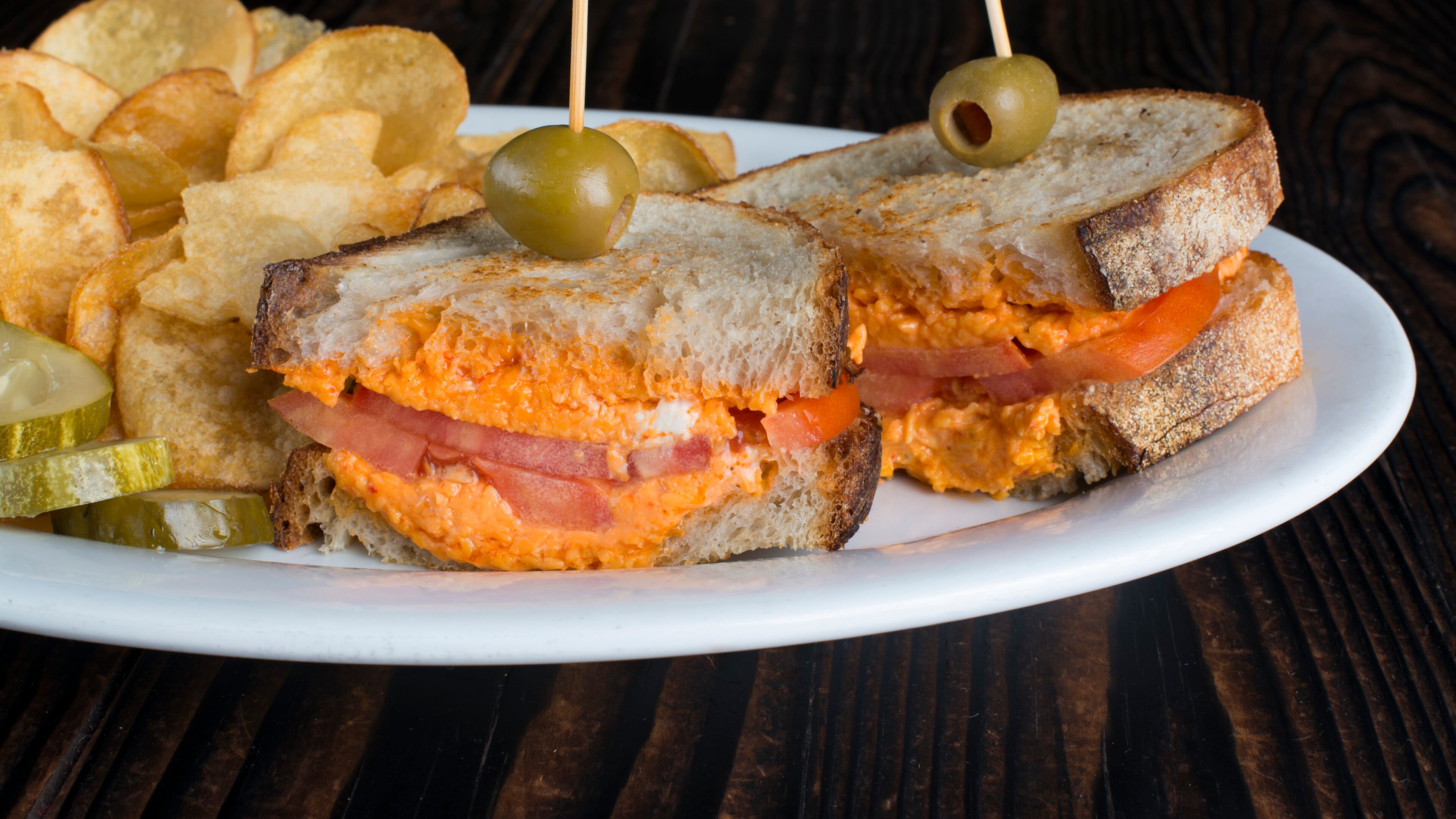 Peach & The Porkchop’s grilled pimento cheese sandwich is served with tomato on sourdough bread, alongside house-made chips. / Photo credit: George Miko Photography