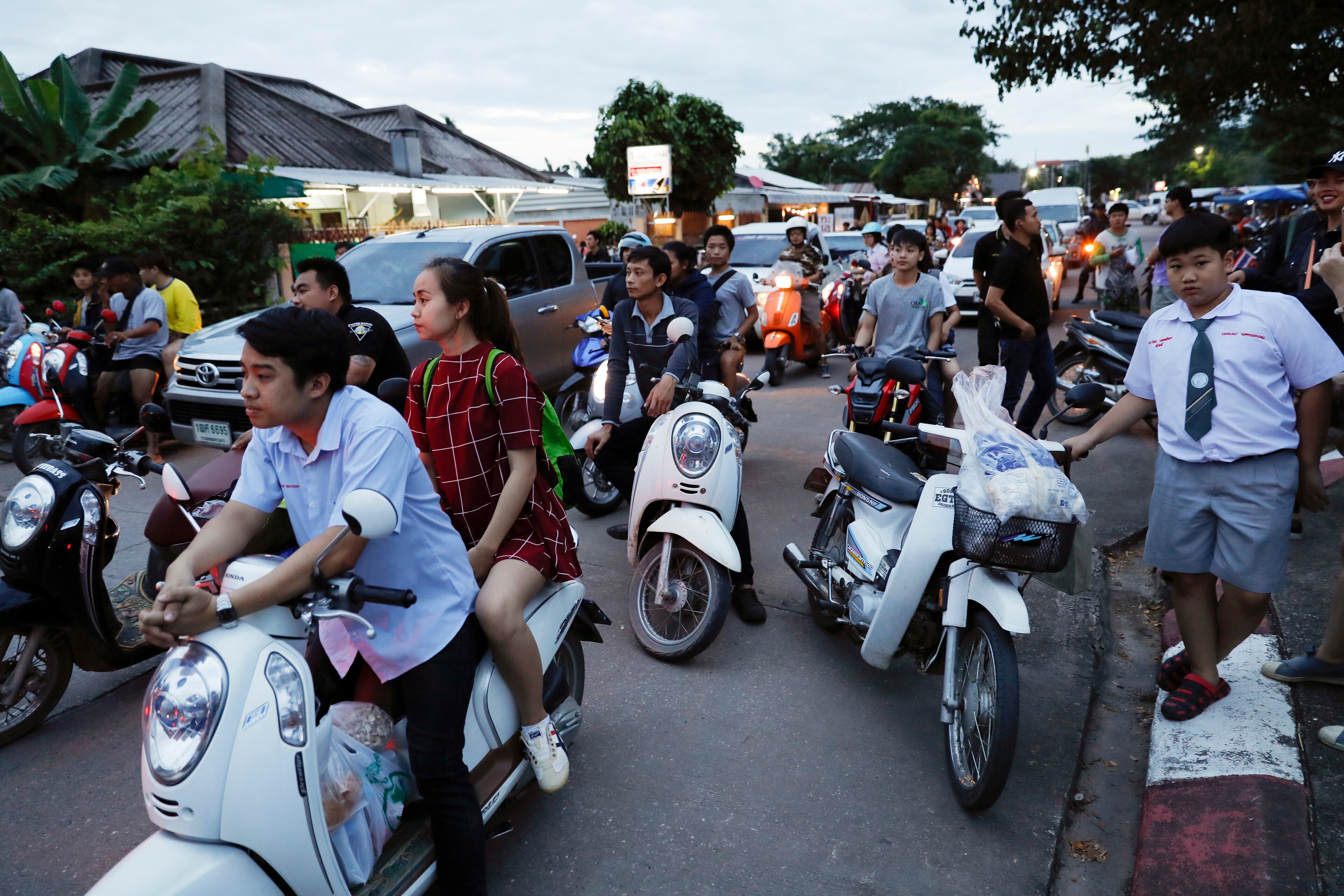 People wait as police block the road during an emergency helicopter evacuation in Chiang Rai as divers evacuated some of the 12 boys and their coach trapped at Tham Luang cave in the Mae Sai district of Chiang Rai province, northern Thailand, Tuesday, July 10, 2018. Thai Navy SEALs say all 12 boys and their coach were rescued from the cave, ending an ordeal that lasted more than 2 weeks. (AP Photo/Vincent Thian)