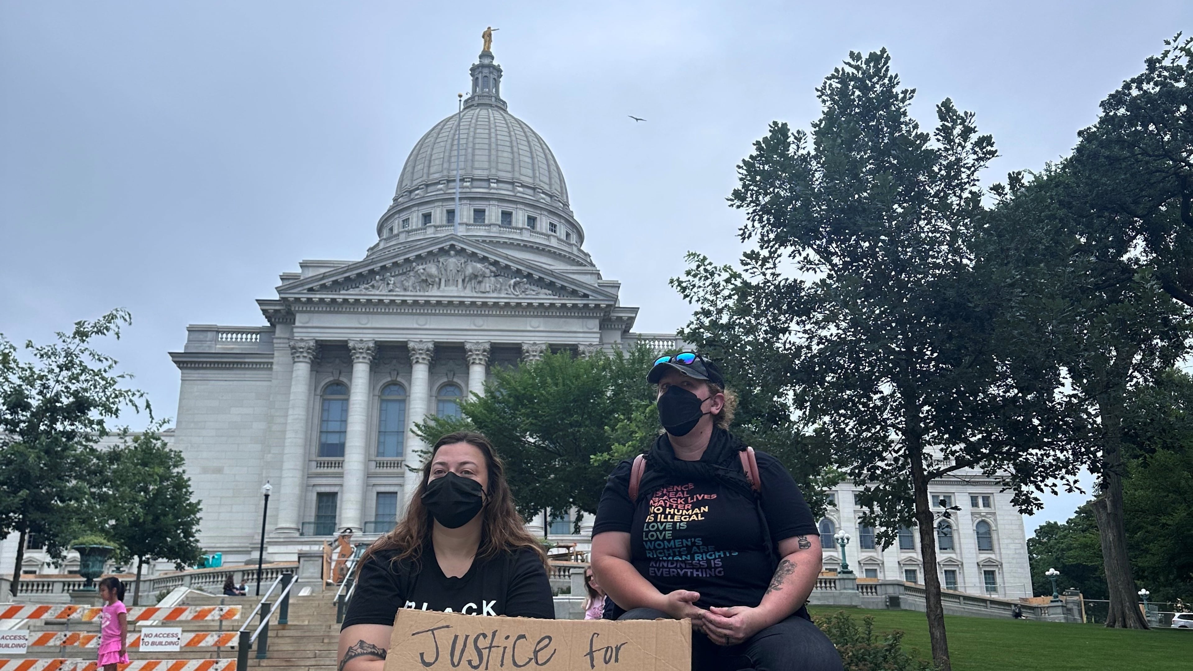 Lilly Nimmer, left, and Reba Bergmann, right, hold a sign to protest the police shooting of Corey Ruiz outside of the Wisconsin state Capitol during the weekly farmers market on Saturday, July 25, 2026, in Madison, Wisconsin. (AP Photo/Scott Bauer)