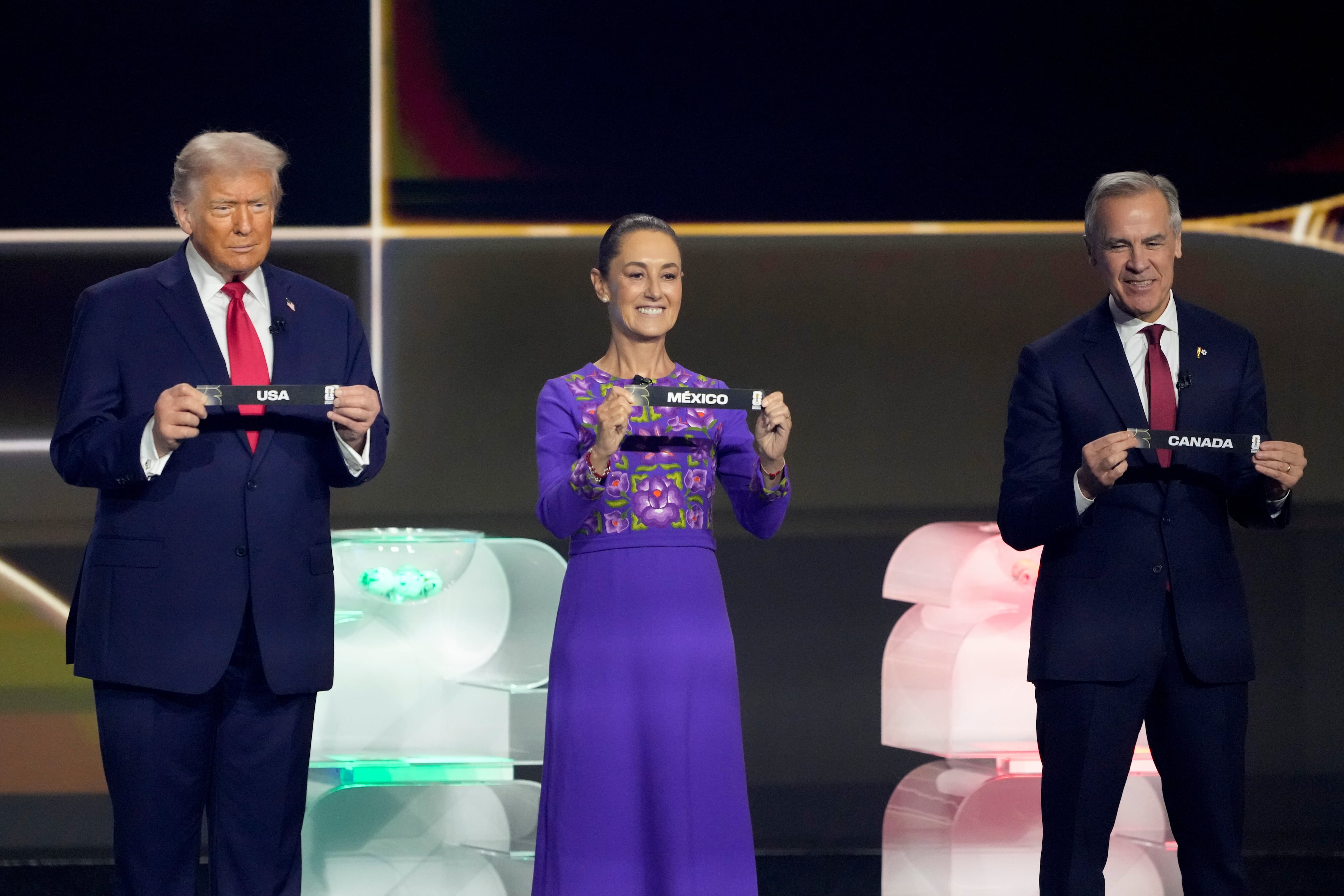 President Donald Trump, Mexican President Claudia Sheinbaum, and Canadian Prime Minister Mark Carney holds their countries' name during the draw for the 2026 soccer World Cup at the Kennedy Center in Washington, Friday, Dec. 5, 2025. (AP Photo/Chris Carlson)
