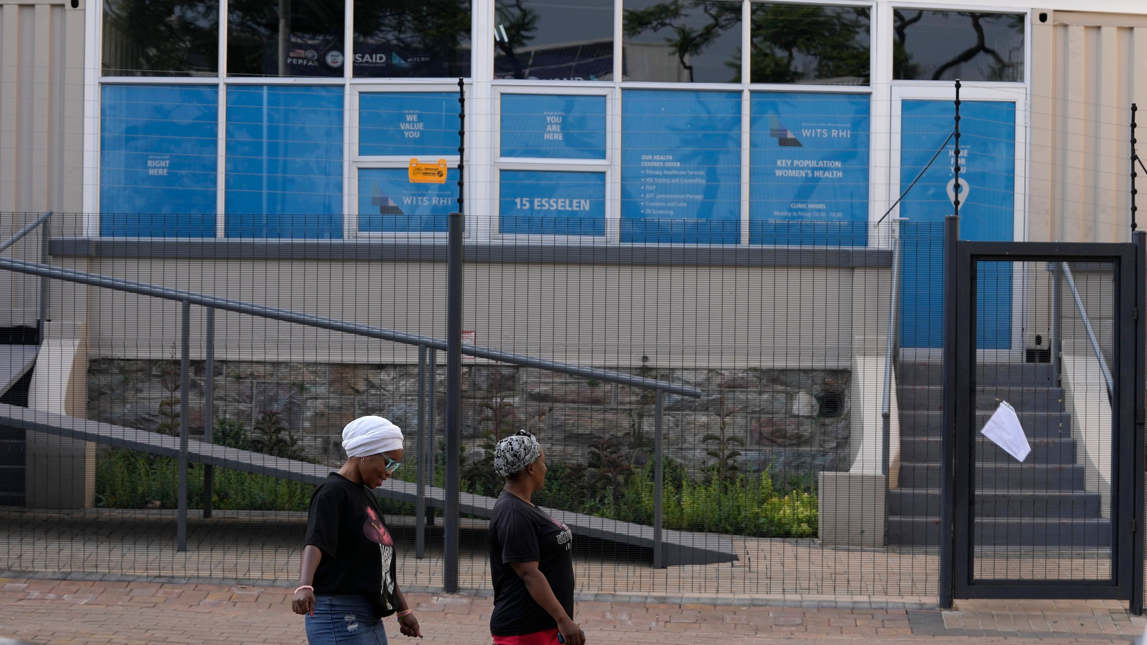 FILE - Women walk past a closed clinic run by WITS Reproductive Health Institute (RHI) as a sign on the gate reads "USAID has served the WITS RHI Key Populations Programme a notice to pause programme implementation. As of Tuesday, 28 January, we are unable to provide services until further notice." in Hillbrow, Johannesburg, South Africa, Feb. 27, 2025. (AP Photo/Themba Hadebe, File)