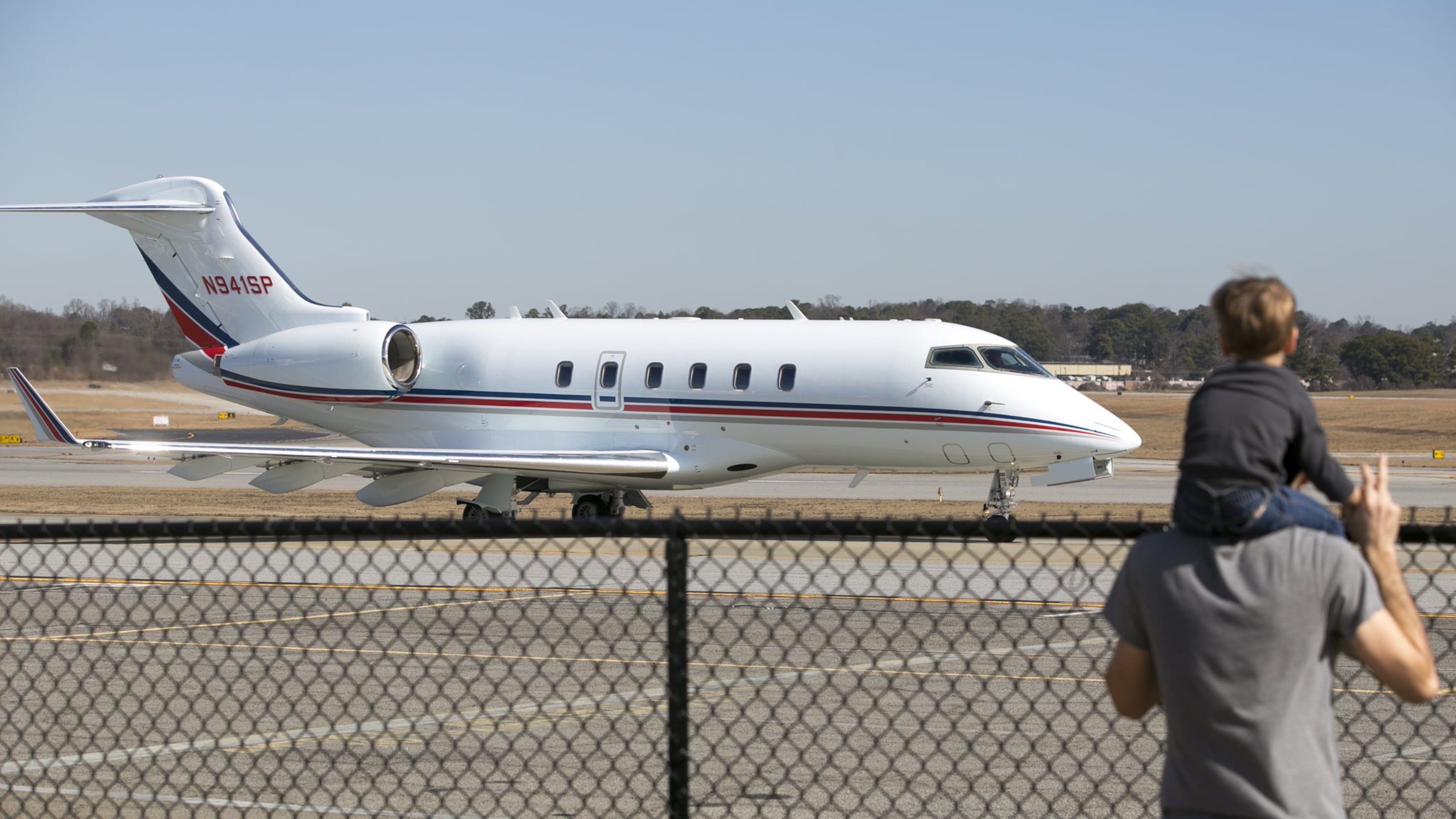 A man and a young boy watch as a private jet moves along the tarmac at DeKalb-Peachtree Airport. (Casey Sykes for The Atlanta Journal-Constitution)