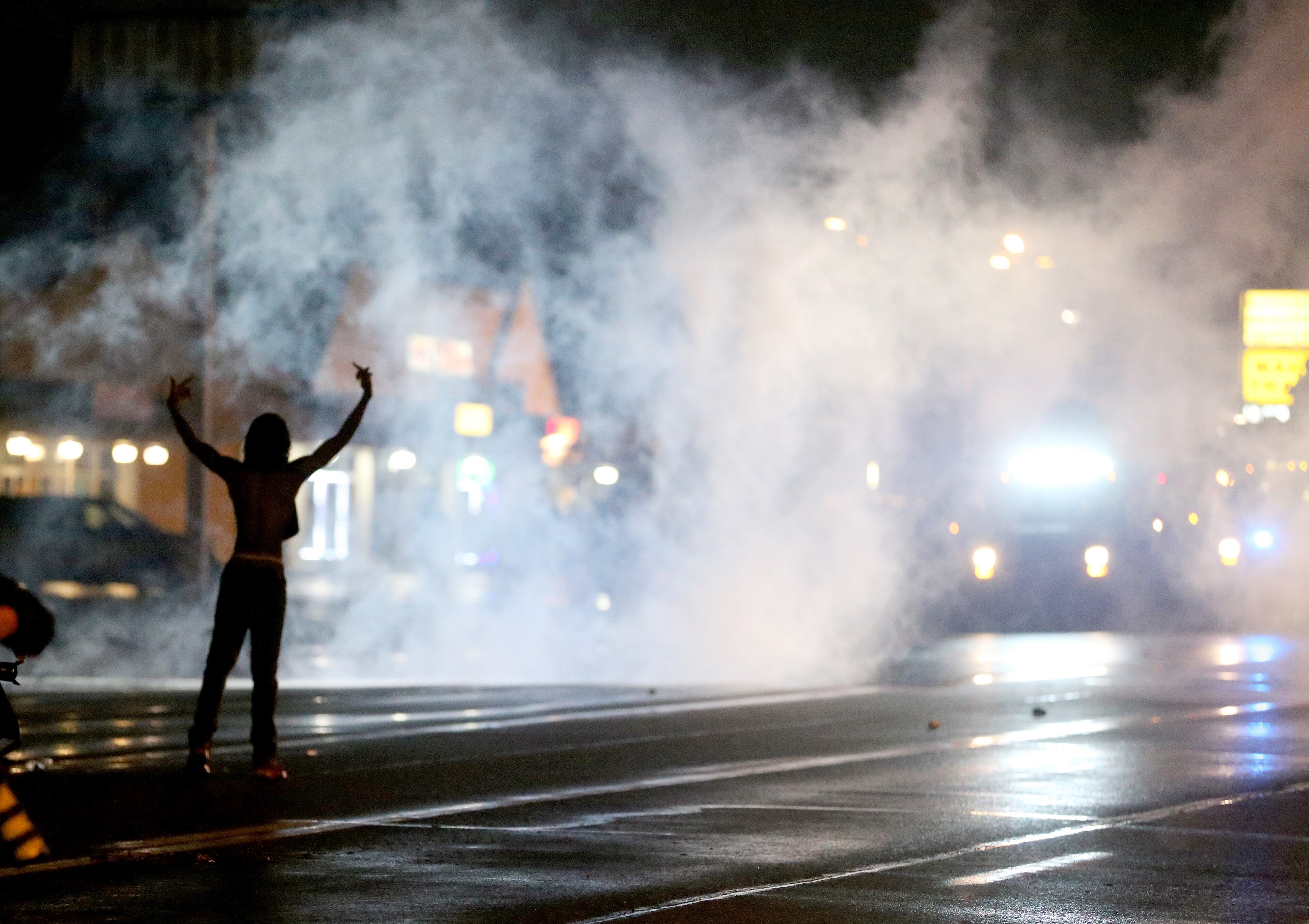 FERGUSON, MO - AUGUST 17: A demonstrator stands near a cloud of tear gas after police fired the gas at demonstrators protesting the shooting death of Michael Brown when they remained on the street after a midnight curfew on August 17, 2014 in Ferguson, Missouri. Police fired smoke bombs and tear gas at protesters who remained on the streets of Ferguson after a Saturday night curfew took effect. Violent outbreaks have taken place in Ferguson since the shooting death of Michael Brown by a Ferguson police officer on August 9th. (Photo by Joe Raedle/Getty Images)