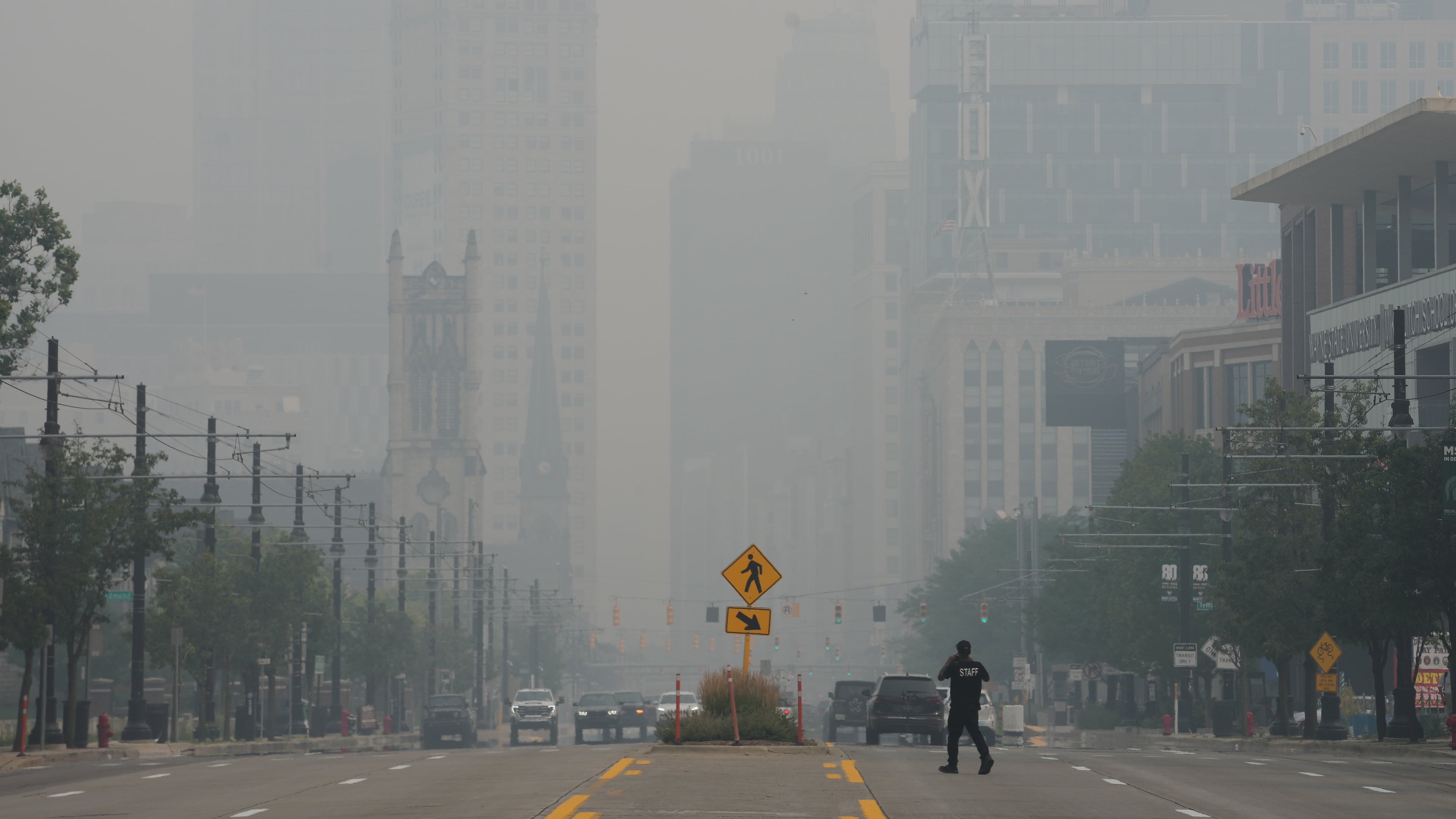 A pedestrian crosses the street as the Detroit city skyline is obscured during poor air quality due to smoke from Canadian wildfires Thursday, July 16, 2026, in Detroit. (AP Photo/Paul Sancya)