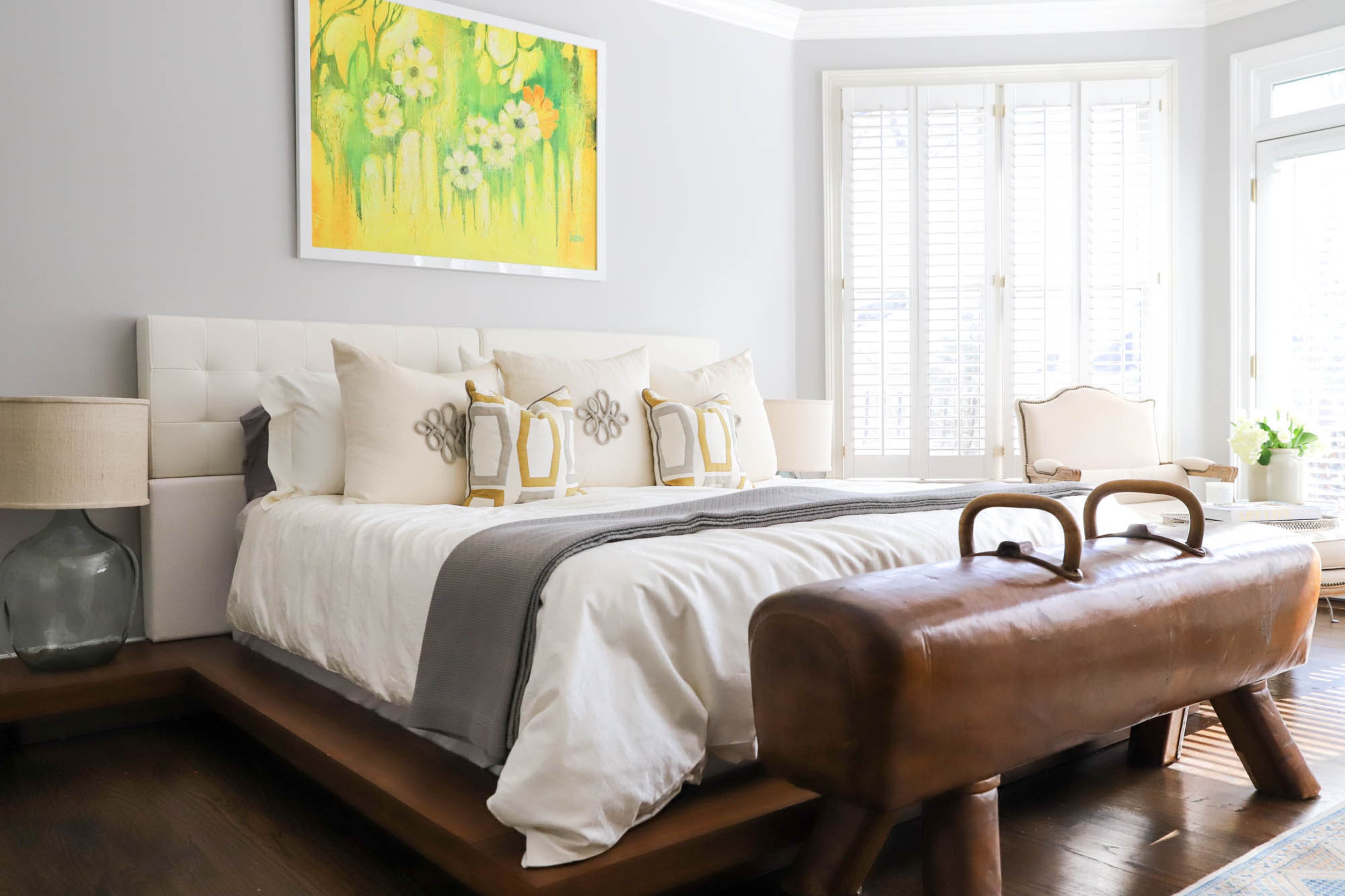 The owner's suite of Joe and Stacy Borocz’s home is open and light, with bed linens from Italy, and decorative pillows from Square Feathers. The oil painting above the bed was passed down to Stacy by her grandmother, and the couple had it reframed to match their style. A German pommel horse serves as a bench at the foot of the bed. Text by Shannon Dominy/Photo by Reynolds Rogers