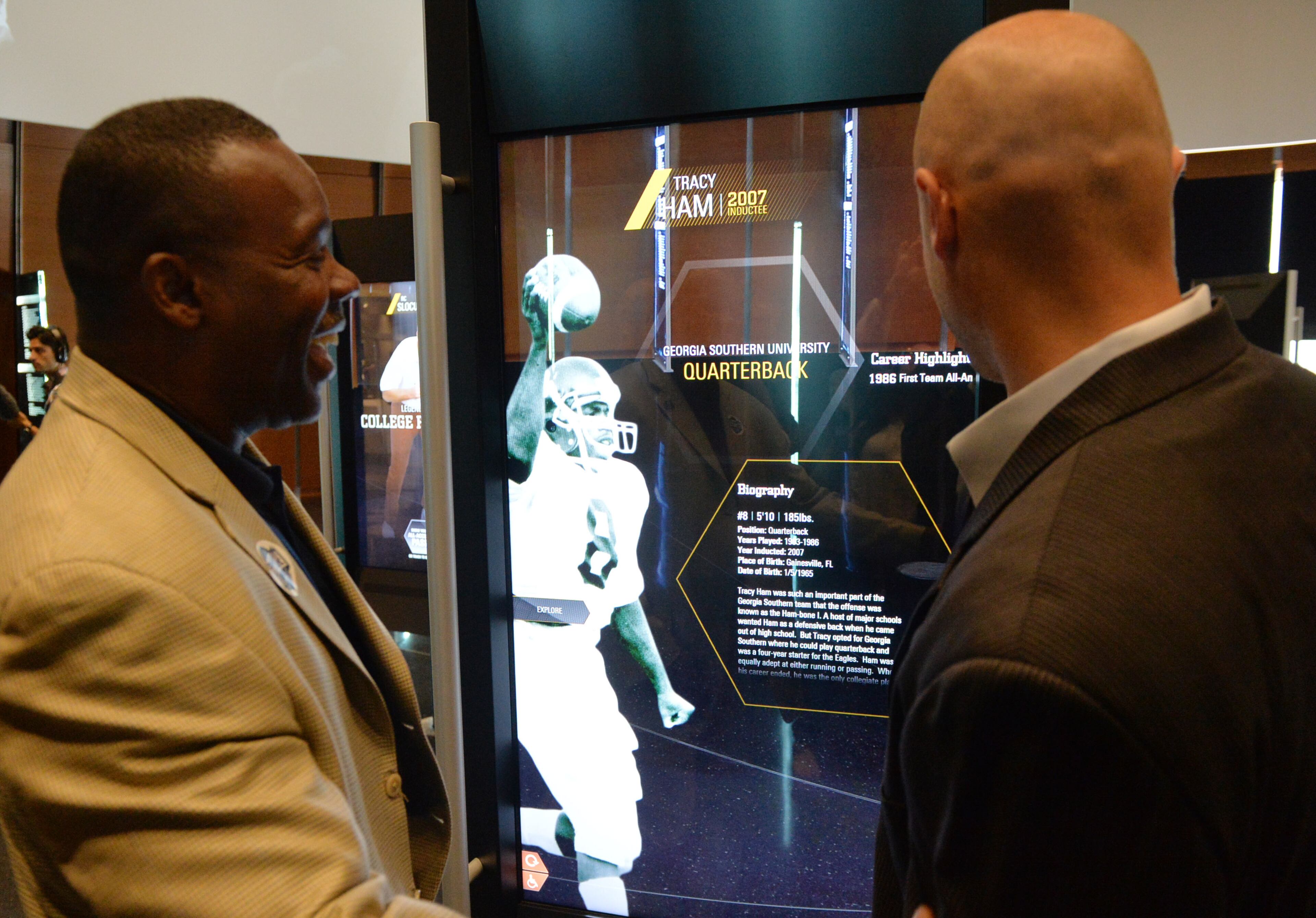 Hall of Fame quarterbacks Tracy Ham (Georgia Southern) and Danny Wuerffel (Florida) look over exhibits in the Hall of Fame area. The displays are RFID-tagged, so they display inductees from the visitor's school upon entering.