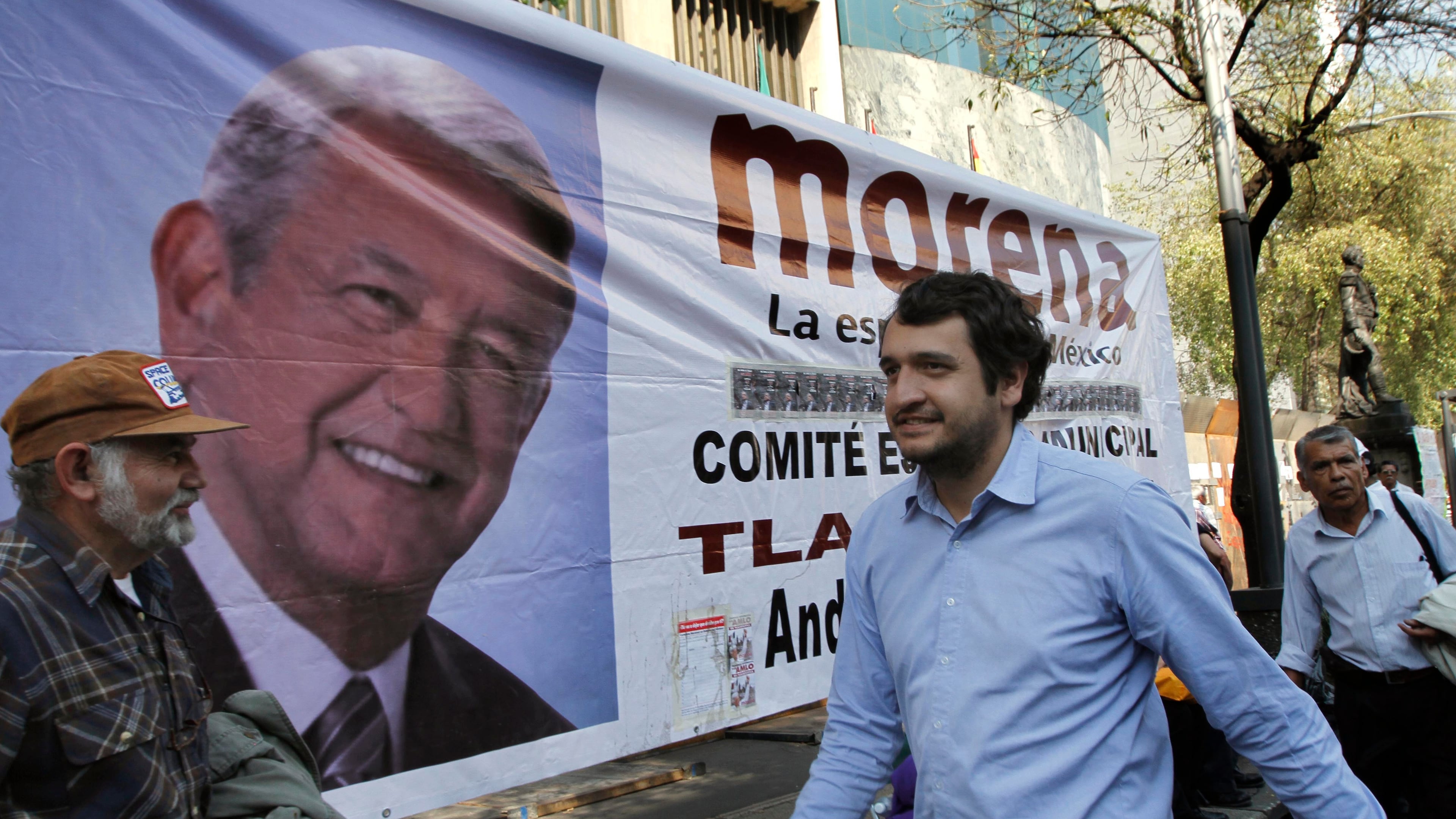FILE - Andres Lopez Beltran, center, walks past a banner featuring an image of his father, Andres Manuel Lopez Obrador, in Mexico City, Dec. 6, 2013. (AP Photo/Marco Ugarte, File)