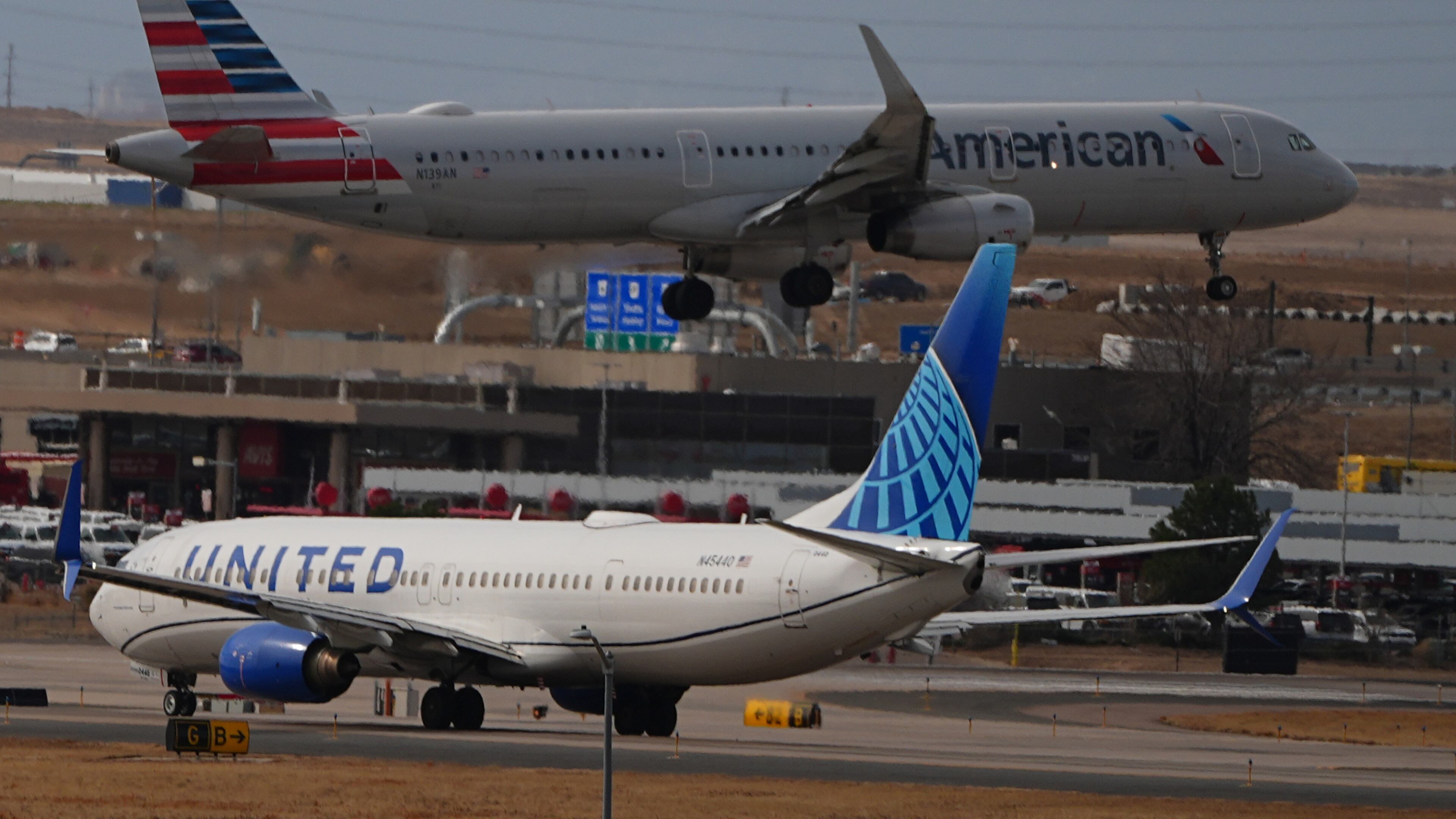 An American Airlines jetliner lands on a runway as a United Airlines plane waits for clearance to take off as high winds strafe Denver International Airport Thursday, March 12, 2026, in Denver. (AP Photo/David Zalubowski)