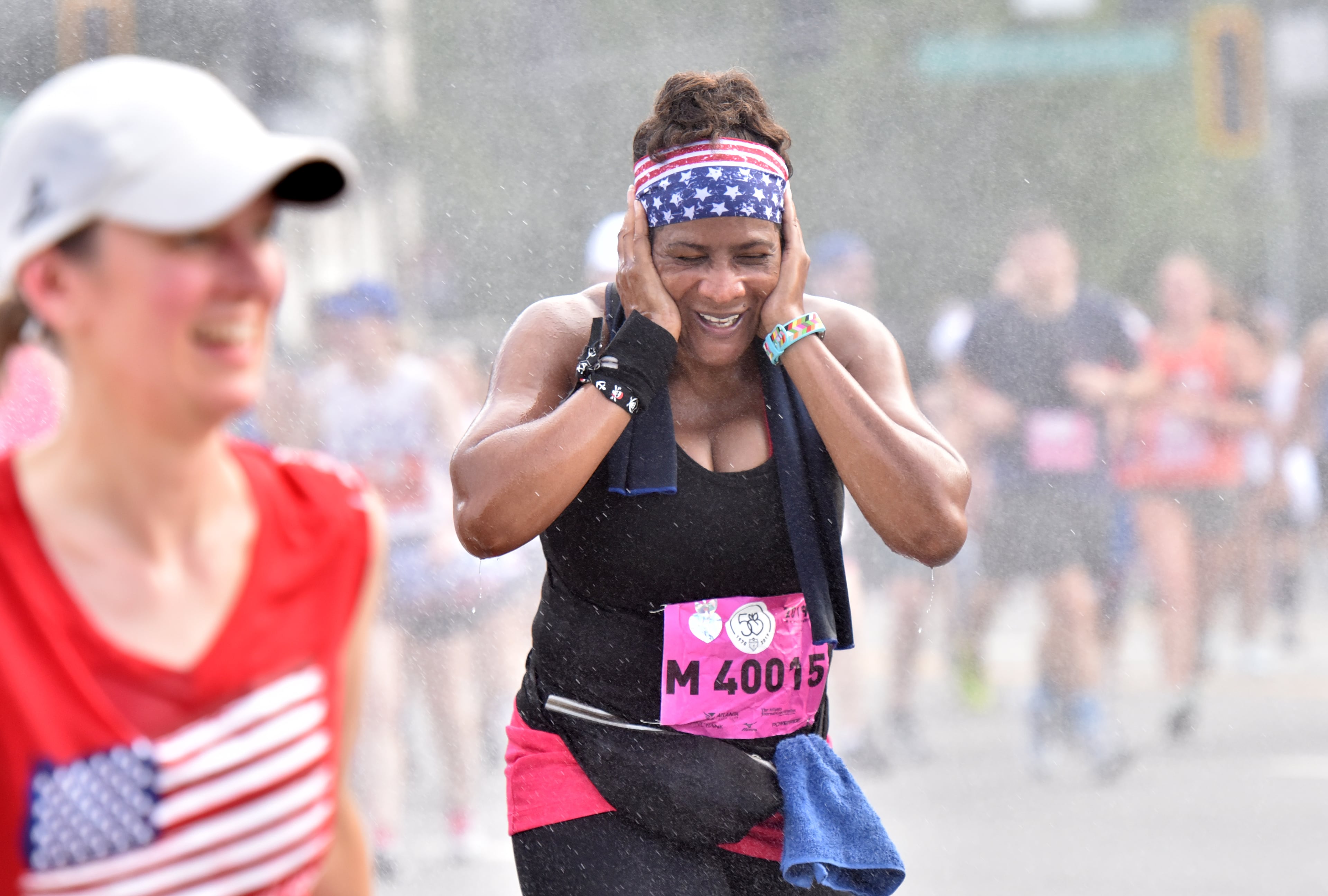 A runner cools off with mist as she makes her way down Peachtree Road during the 50th AJC Peachtree Road Race on Thursday, July 4, 2019. (Hyosub Shin / Hyosub.Shin@ajc.com)