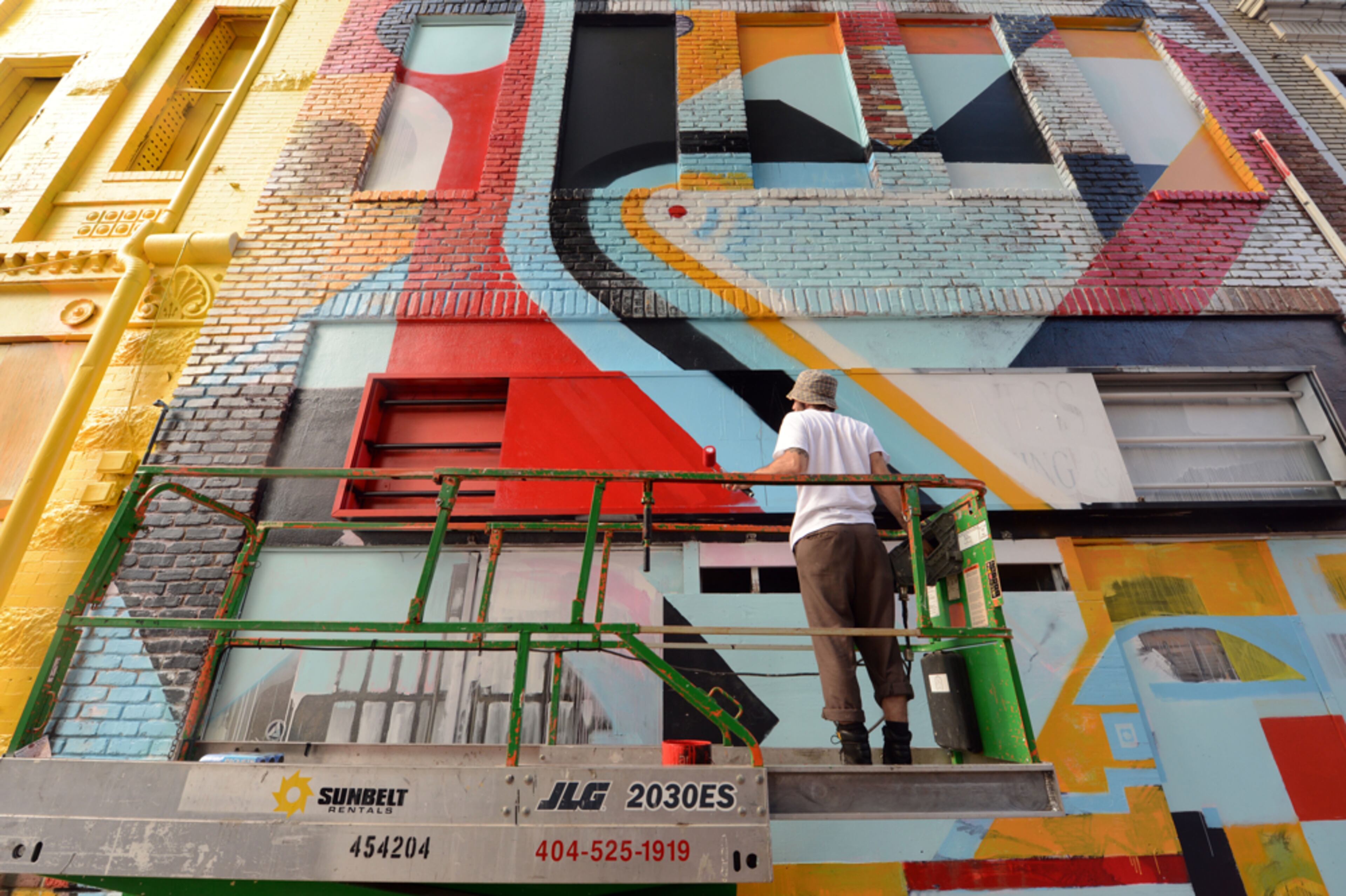 Street artists painting buildings in vibrant colors and strong shapes, what's NOT to like about shooting that? October 26, 2012 ATLANTA Mural artist Born works on a mural on Broad Street Friday afternoon. Elevate South Broad Mural Project: Entire Block Gets An Artistic Facelift! The City of Atlanta Office of Cultural Affairs is presenting Elevate, a contemporary art series, all this week in downtown Atlanta. Five world-class muralists are painting an entire block of buildings on South Broad Street! Visitors and residents of the area are watching the work of artists Hense, Tilt, Push, Sever and Born as they transform the neighborhood. All the artists will be there tomorrow afternoon from Noon-6 pm up on lifts, busily working on the project.For more details: http://www.ocaatlanta.com/Elevatesouthbroad KENT D. JOHNSON / AJC