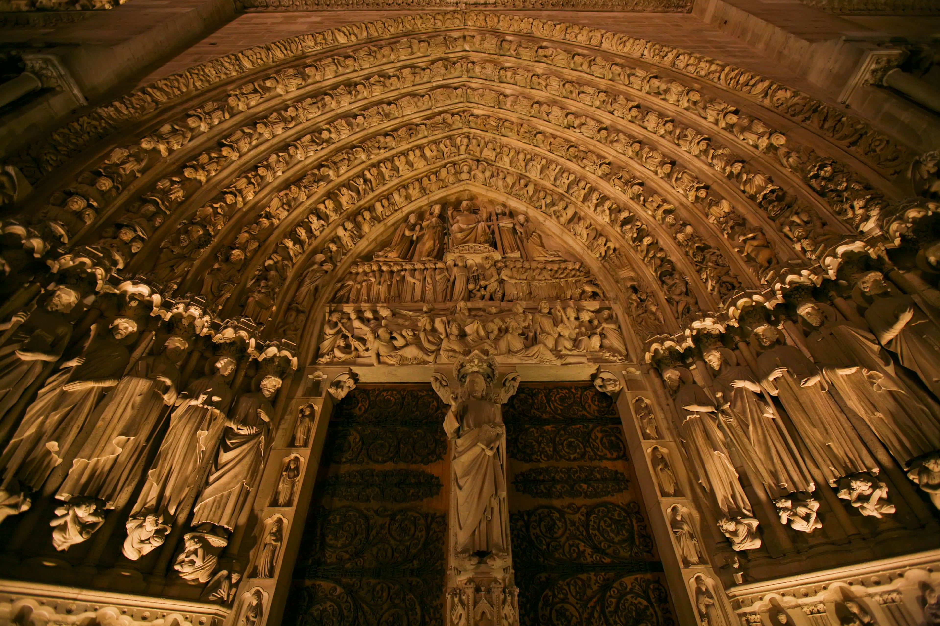 Notre Dame de Paris is a historic Roman Catholic Marian cathedral on the eastern half of the Île de la Cité in the fourth arrondissement of Paris, France. Widely considered one of the finest examples of French Gothic architecture and among the largest and most well-known churches in the world, Notre Dame is the cathedral of the Catholic Archdiocese of Paris; that is, it is the church that contains the cathedra (official chair) of the Archbishop of Paris, currently André VingtTrois. The cathedral treasury is notable for its reliquary, which houses the purported crown of thorns, a fragment of the True Cross and one of the Holy Nails. Notre Dame de Paris is often reputed to be one of the most prominent examples of Gothic architecture in both France and in Europe as a whole, and the naturalism of its sculptures and stained glass are in contrast with earlier Romanesque architecture. The first period of construction from 1163 into 1240s coincided with the musical experiments of the Notre Dame school. The cathedral suffered desecration during the radical phase of the French Revolution in the 1790s, when much of its religious imagery was damaged or destroyed. An extensive restoration removed remaining decoration, returning the cathedral to an 'original' gothic state.