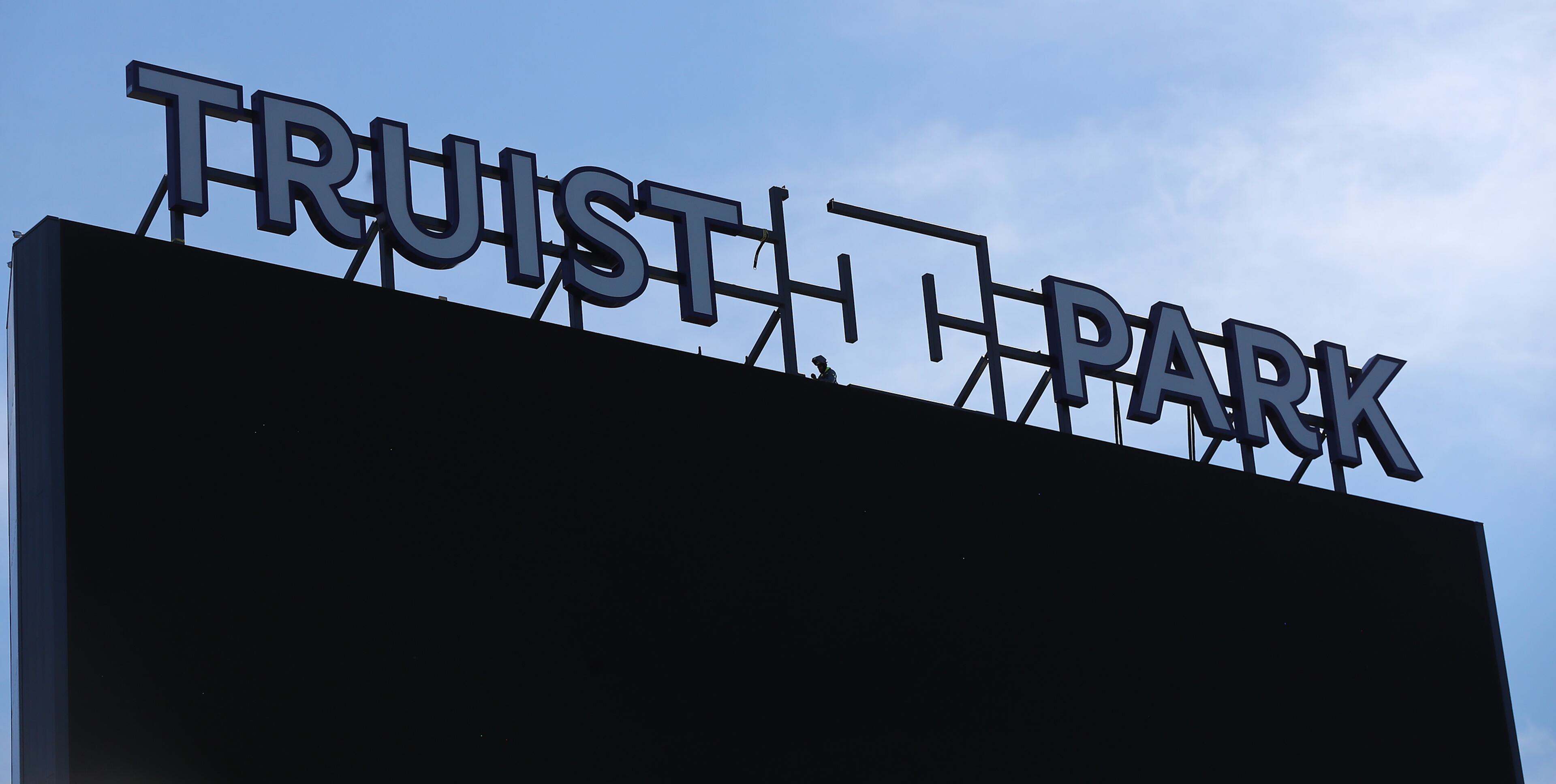 A constuction worker installs the new sign over the center -field scoreboard/video board at newly renamed Truist Park.