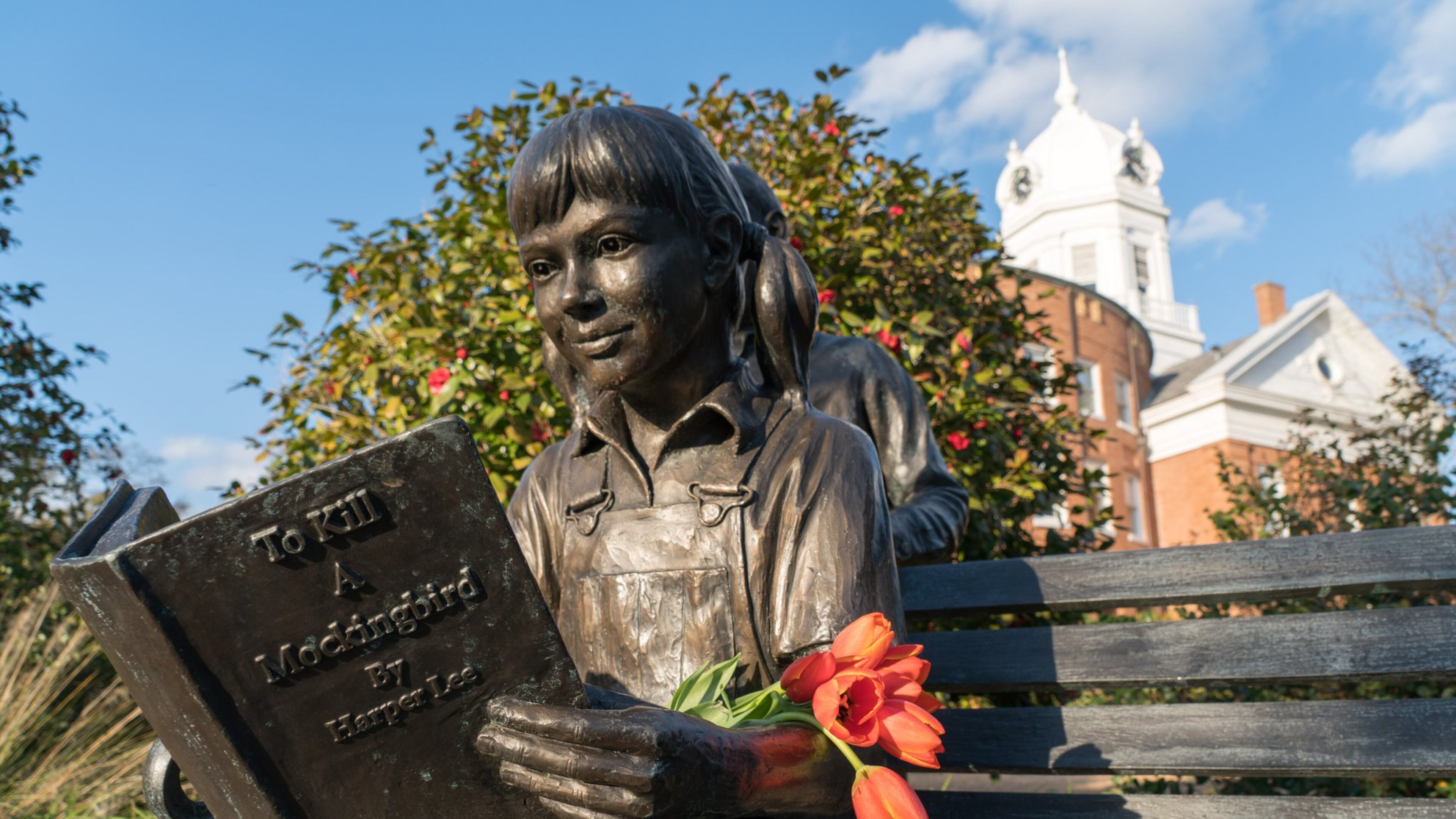 Flowers left on a statue in Monroeville, Ala., the hometown of Harper Lee, on the day of her death, Feb. 19, 2016. Lee’s death at 89 struck a chord around the world, but nowhere did it resonate as deeply as in the town where she grew up and set her masterpiece, “To Kill a Mockingbird.” Schools in Biloxi, Mississippi banned the book this week. (Jeff Haller/The New York Times)