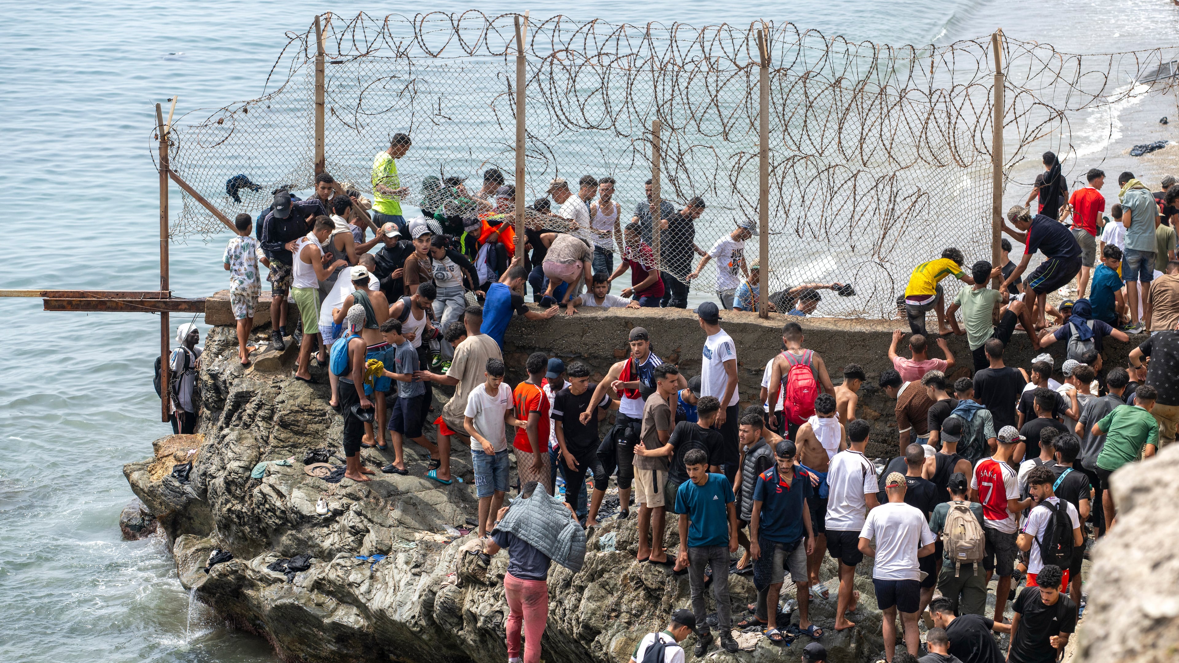 People breach barbed wires as they attempt to cross from the Moroccan northern town of Fnideq to the Spanish enclave of Ceuta, Friday, July 31, 2026. (AP Photo)