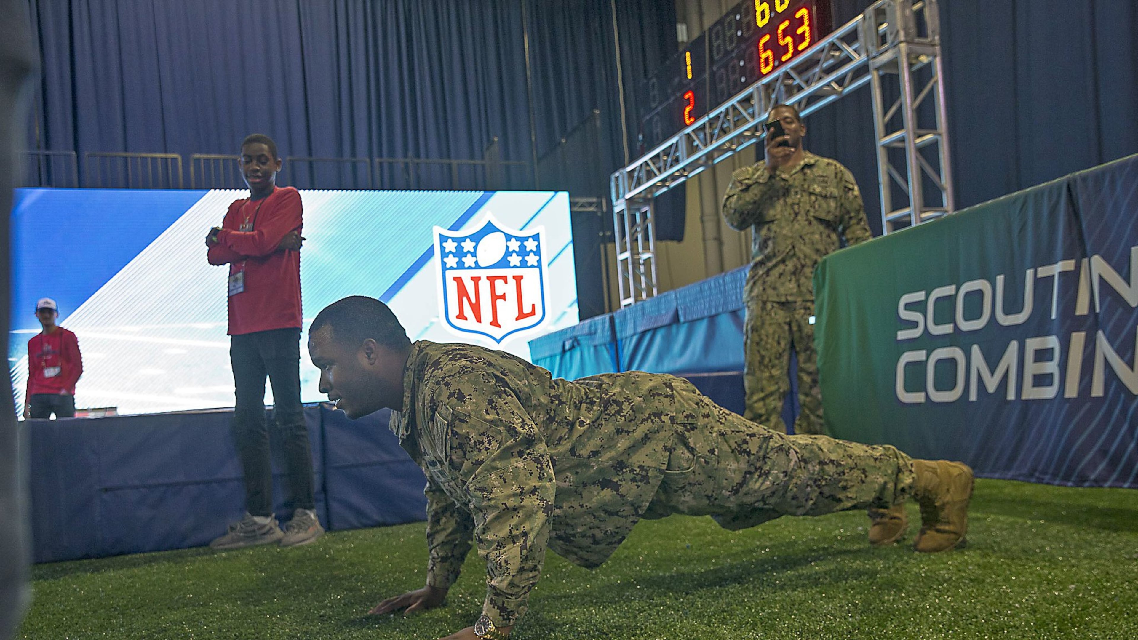 U.S. Navy Petty Officer first class Dchuan Parker (center) completes a set of 20 push-ups after losing a race to U.S. Navy Petty Officer second class Michael Walker (right) during the Super Bowl LIII Fan experience Salute to Military day at the Georgia World Congress Center in Atlanta, Monday, January 28, 2019.