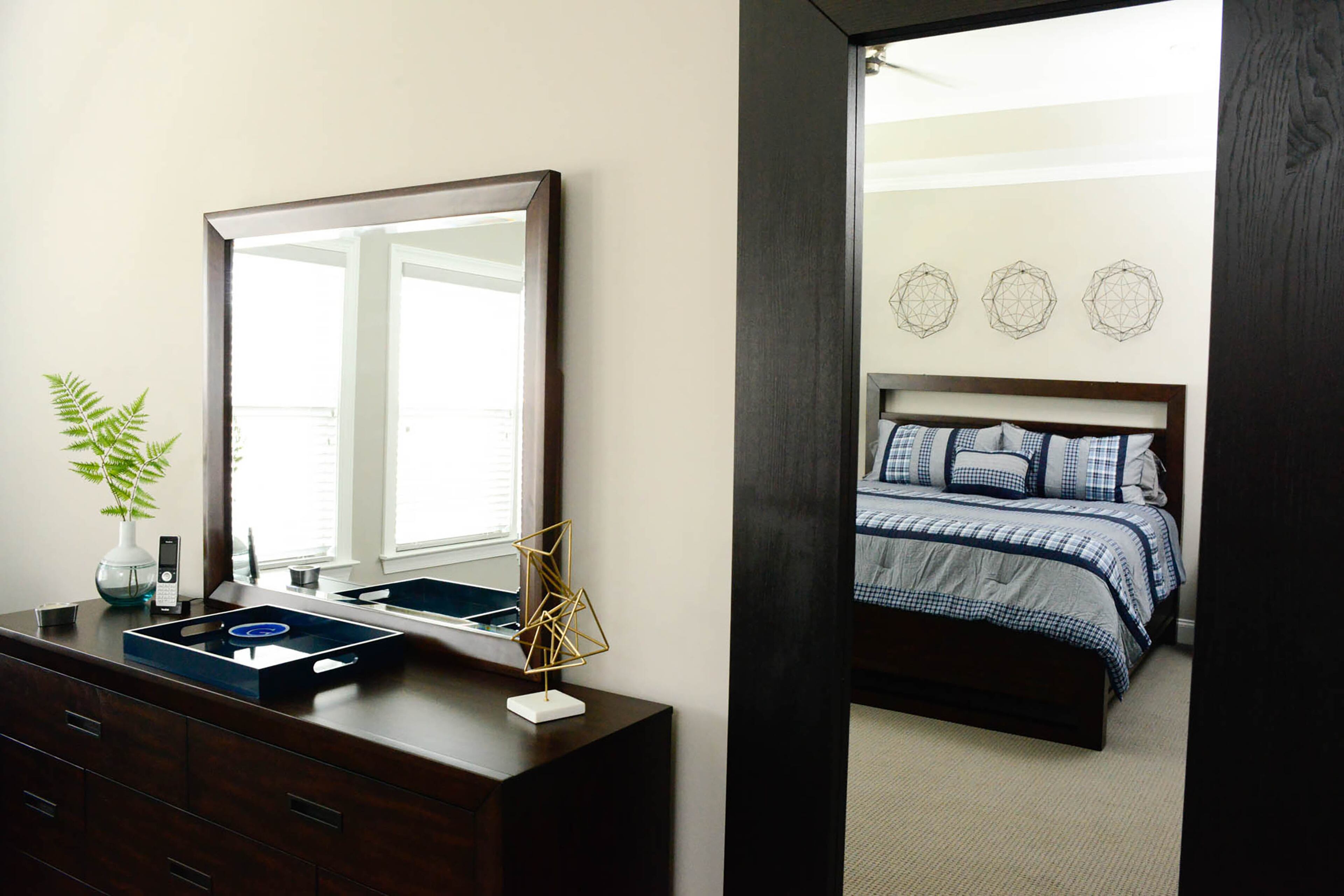 The mirror and dresser, from Living Spaces' Tesla series, has a walnut finish that adds warmth to the master bedroom walls, painted in Requisite Gray by Sherwin-Williams. The wall mirror, framed in a dark finish, is from Ikea.