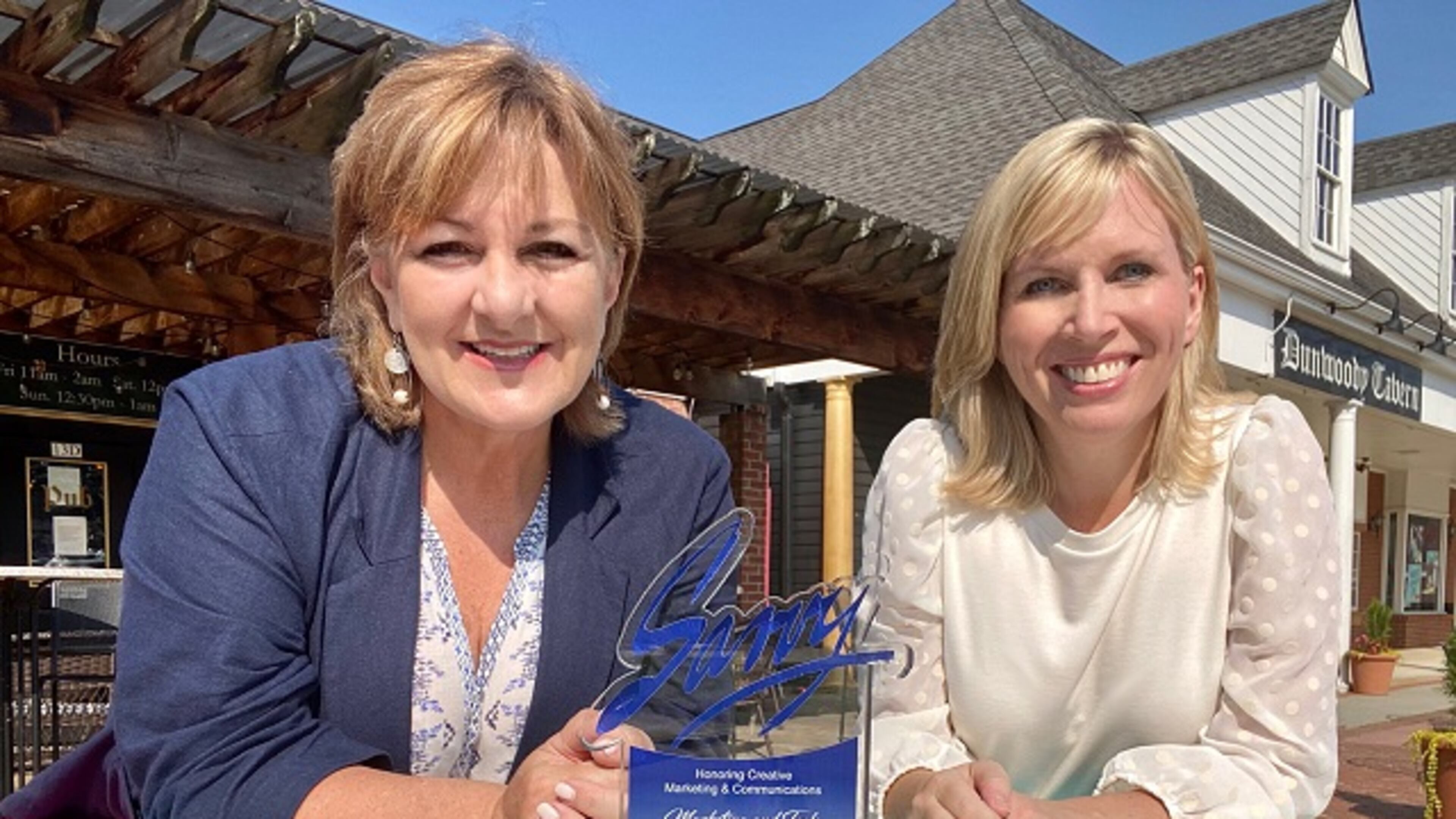 Dunwoody Communications Manager Kathy Florence and Dunwoody Communications Director Jennifer Boettcher pose with the Savvy Award at a painted picnic table in the Dunwoody Village. CONTRIBUTED