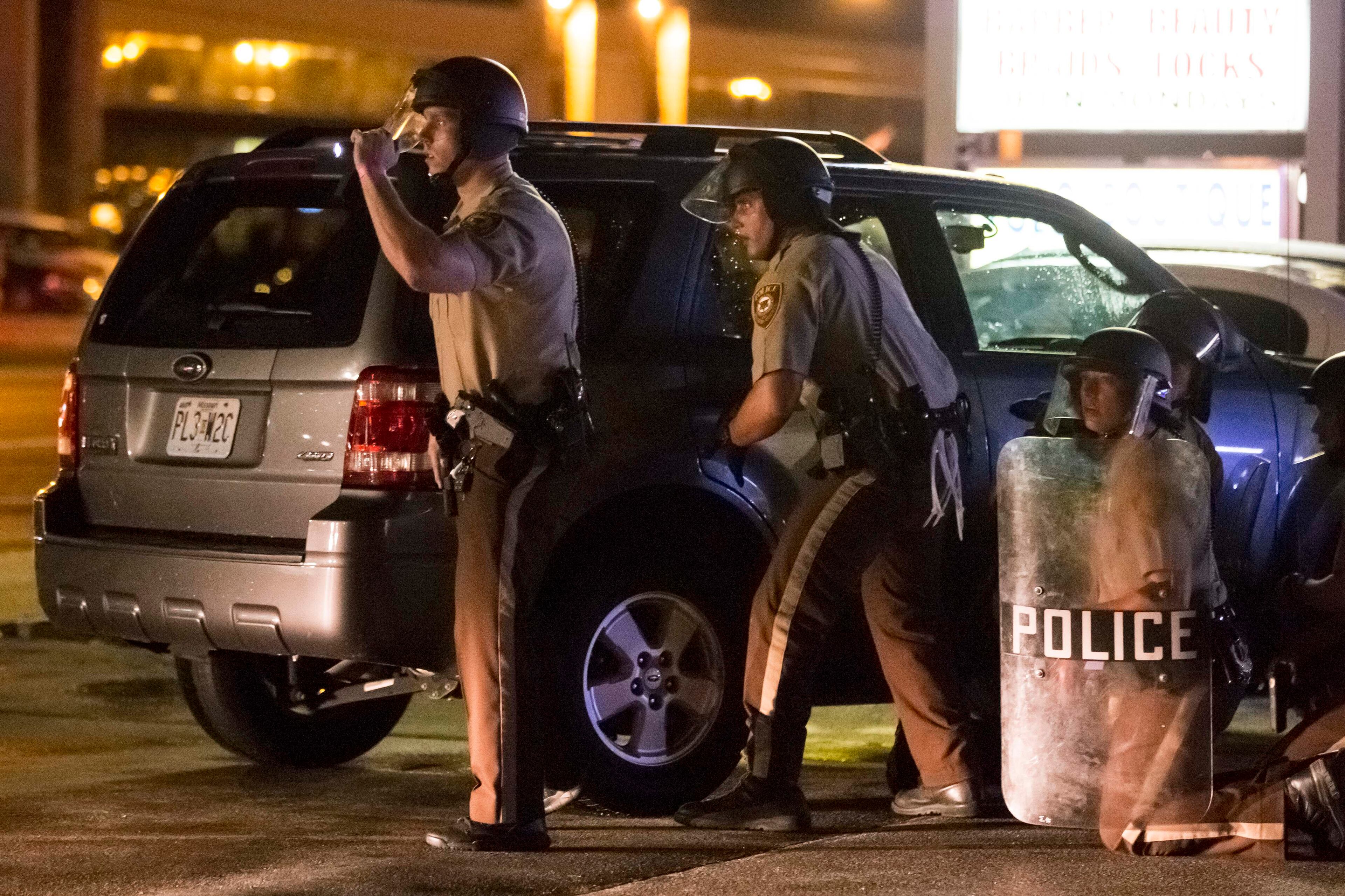 Police officers take cover after shots were fired following a vigil for Michael Brown on West Florissant Avenue in Ferguson, Mo., Aug. 9, 2015. A day of peaceful protest commemorating the killing of an unarmed black teenager by a white police officer one year ago ended in gunfire late Sunday. A St. Louis County police officer was involved in the shooting, the department said. (Whitney Curtis/The New York Times)