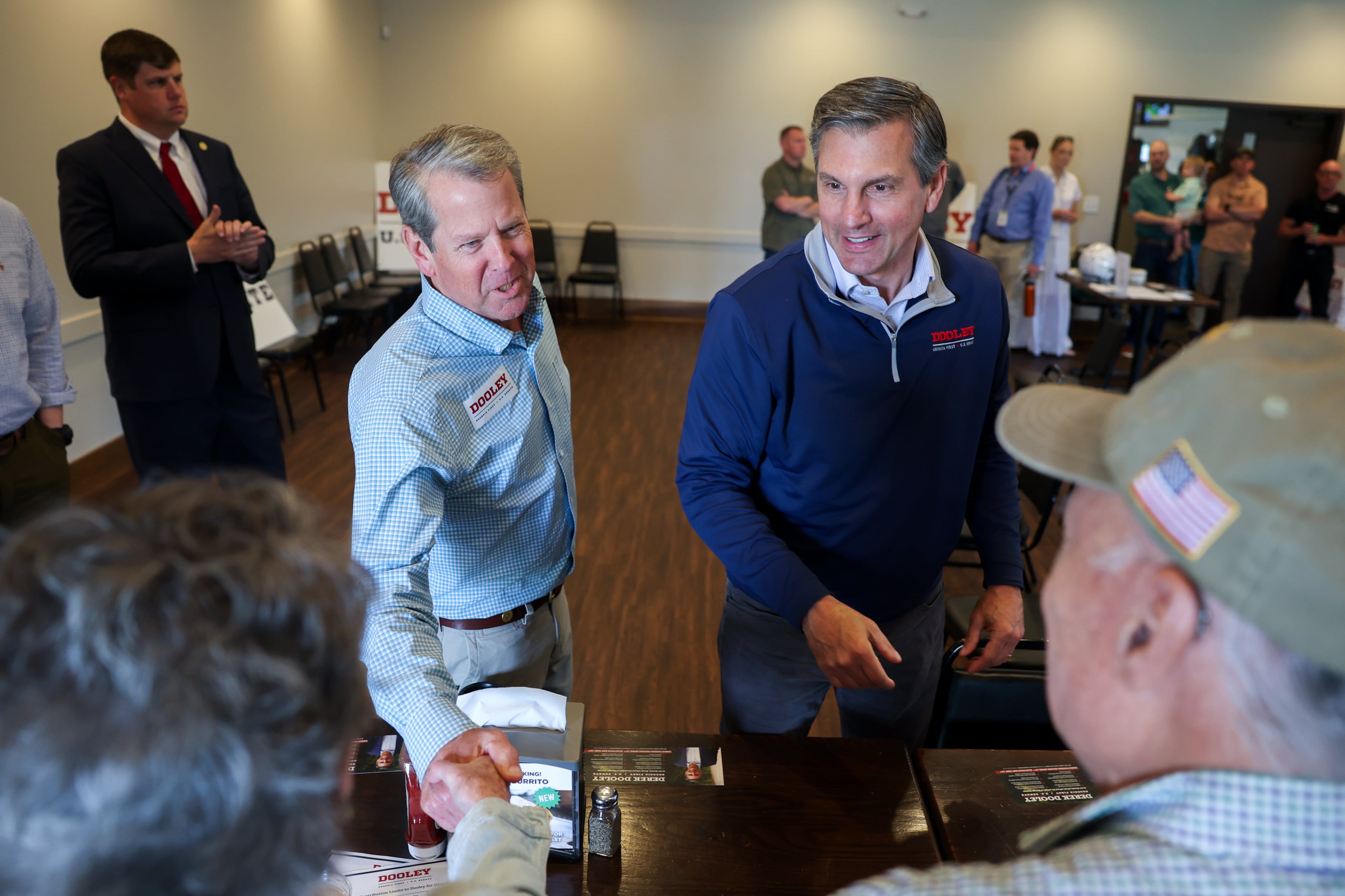 Gov. Brian Kemp, center left, and Republican U.S. Senate candidate Derek Dooley greet supporters at campaign stop for Dooley at Farmview Market in Madison, Ga., on May 8, 2026. (Arvin Temkar/AJC)