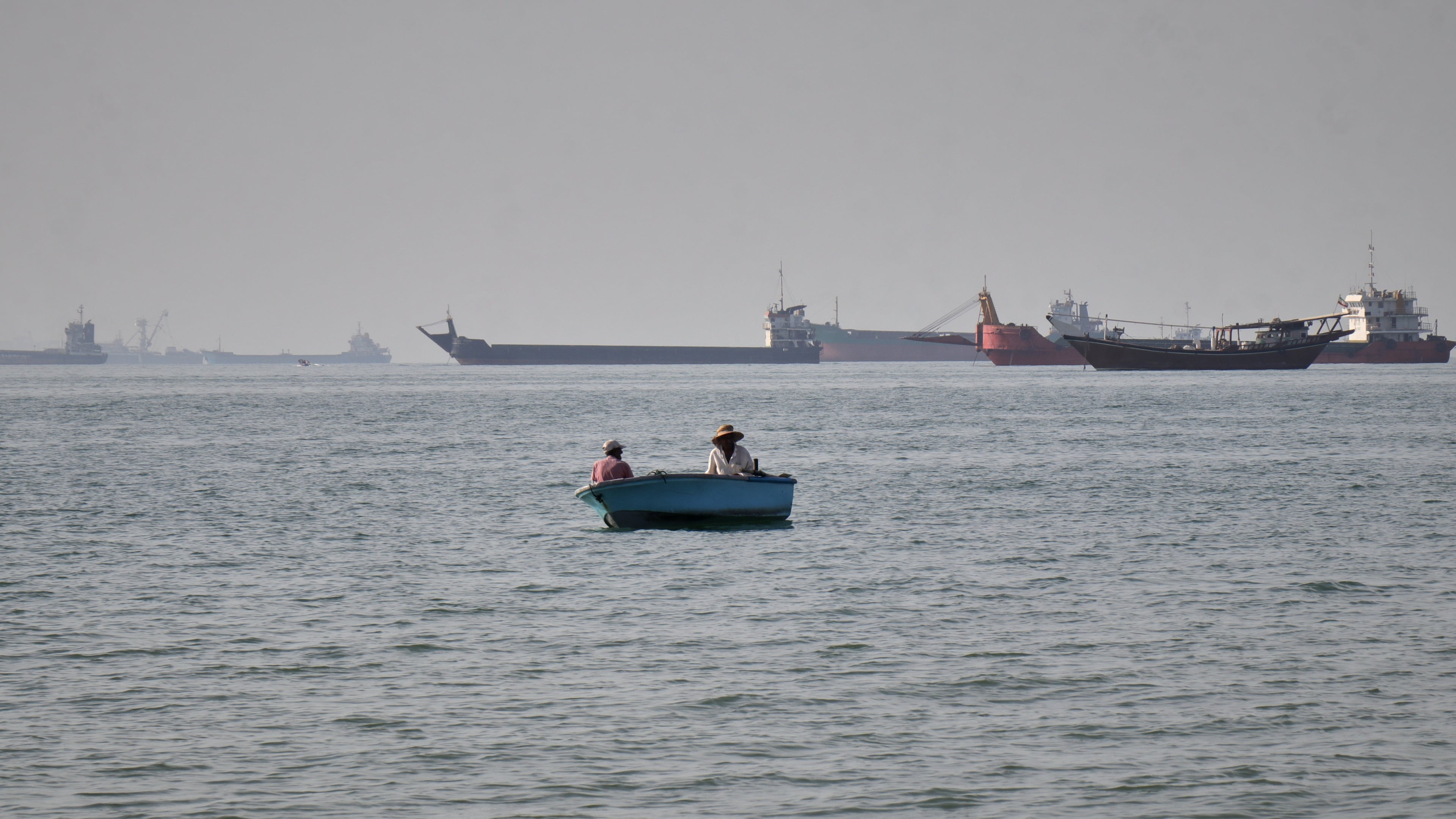 Two men sit in a small boat on the water as a mix of bulk carriers, cargo ships, and service vessels line the horizon in the Strait of Hormuz off Bandar Abbas, Iran, Monday, April 27, 2026.(Razieh Poudat/ISNA via AP)