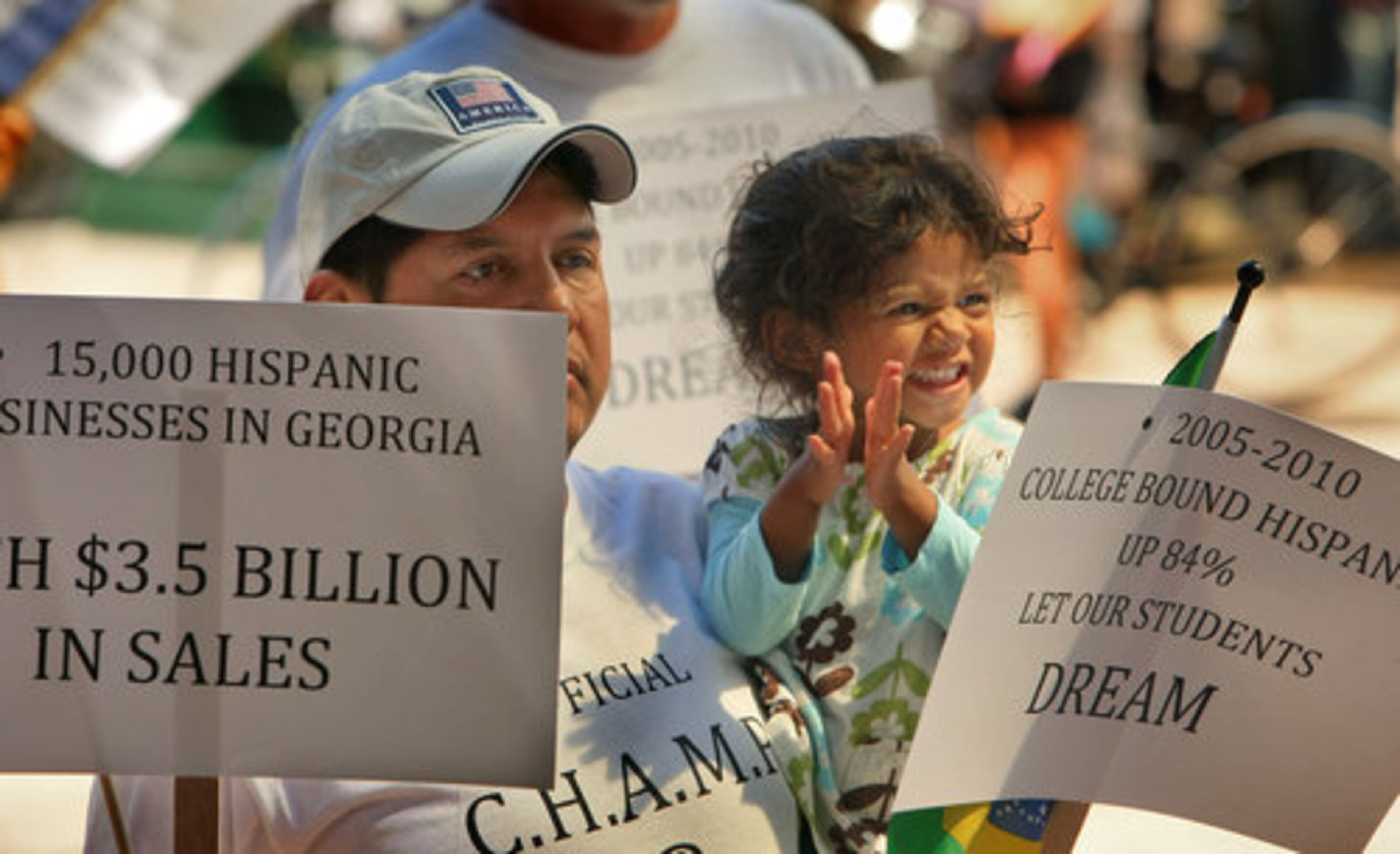 Eosabio Camargo (left) of Marietta holds 3-year old daughter, Gabriella and signs during the rally at Woodruff Park Monday.