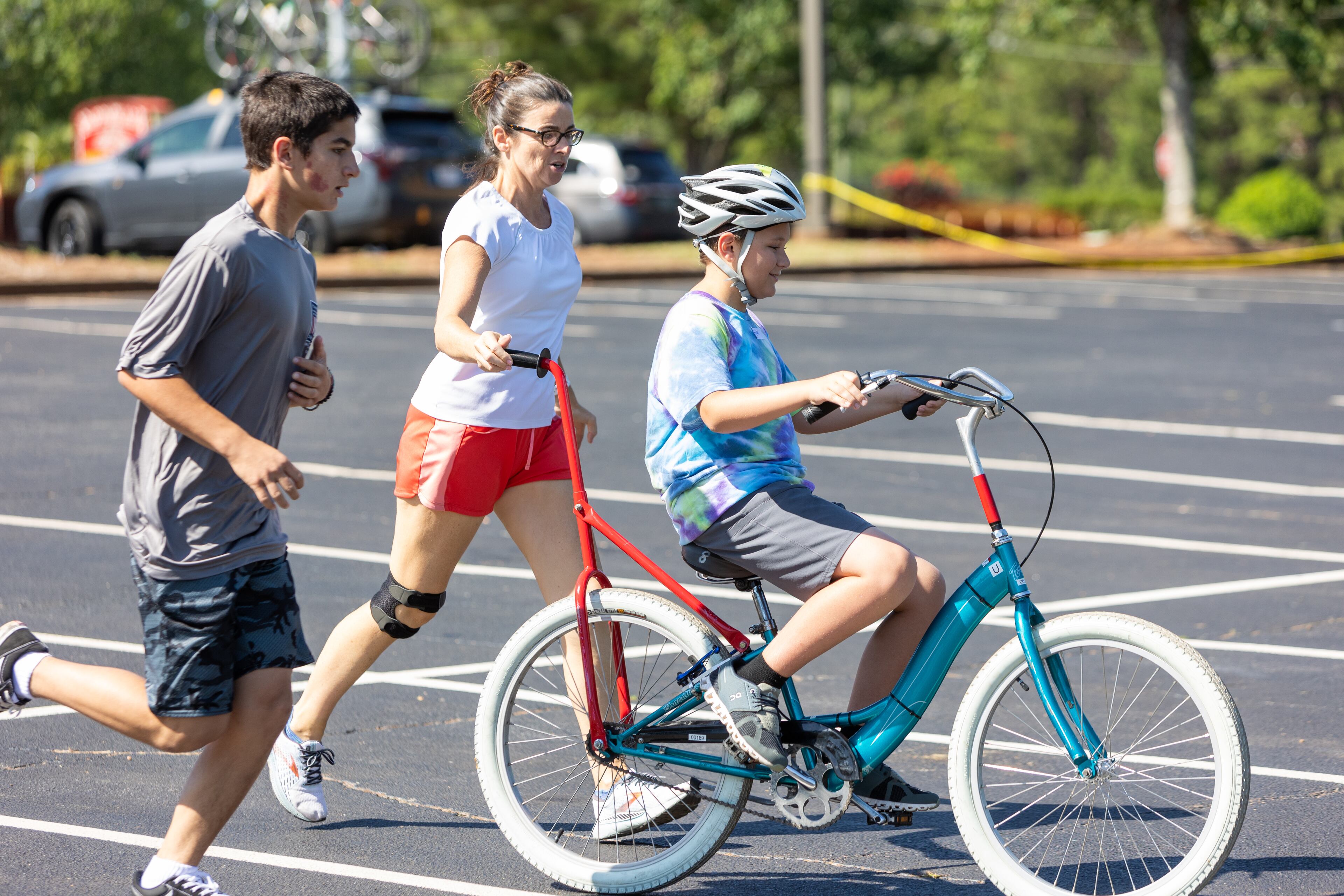 Volunteers Jack Reagin and Niam Goggin helped special-needs camper Rylan learn how to ride a two-wheel bike without adaptations during the iCan Bike Alpharetta camp at The Cooler in Alpharetta. PHIL SKINNER FOR THE ATLANTA JOURNAL-CONSTITUTION.