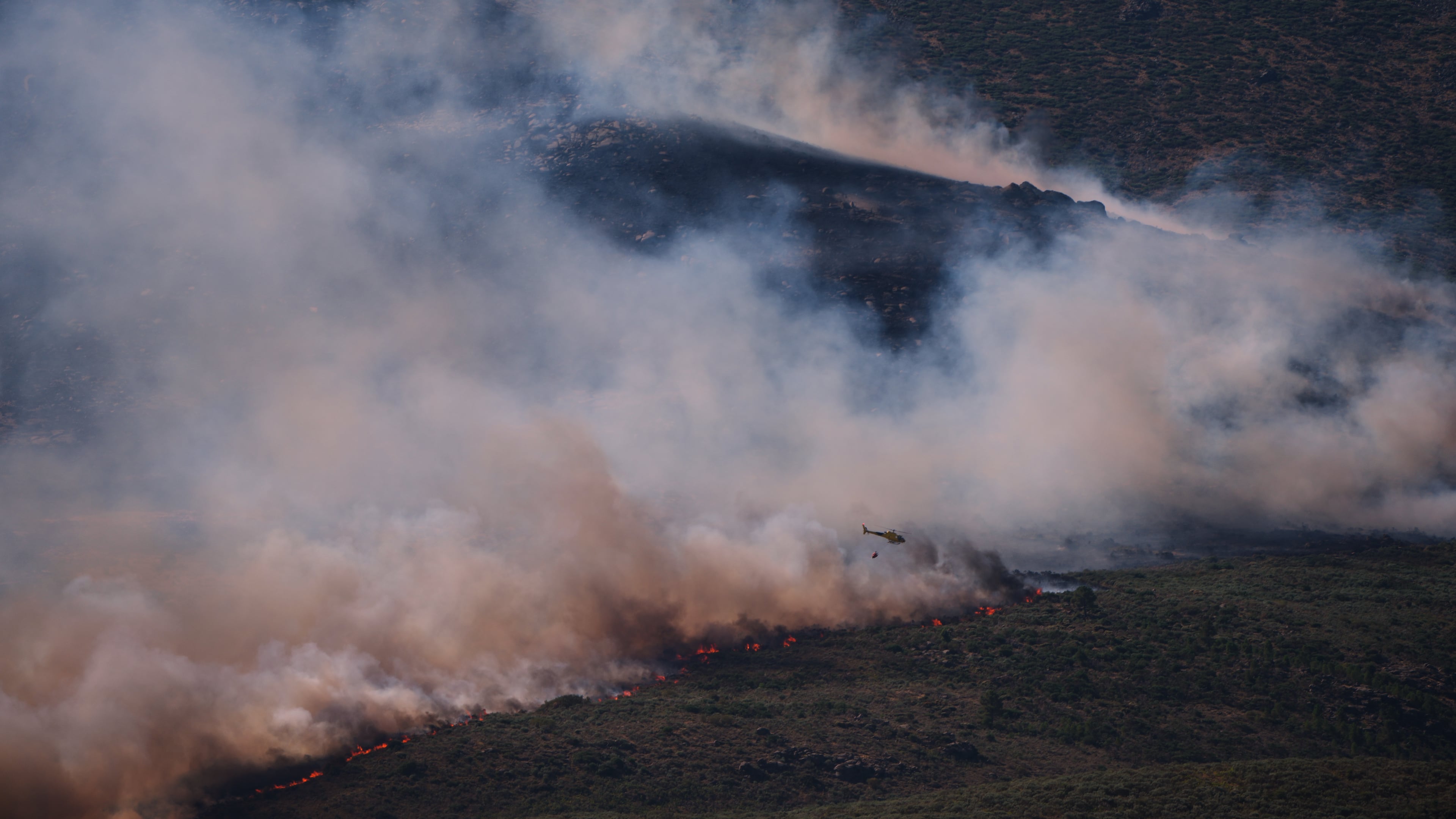 A firefighting helicopter drops water on the flames as a wildfire advances near Burgohondo, Ávila province, Spain, Friday, July 24, 2026. (AP Photo/Manu Fernandez)