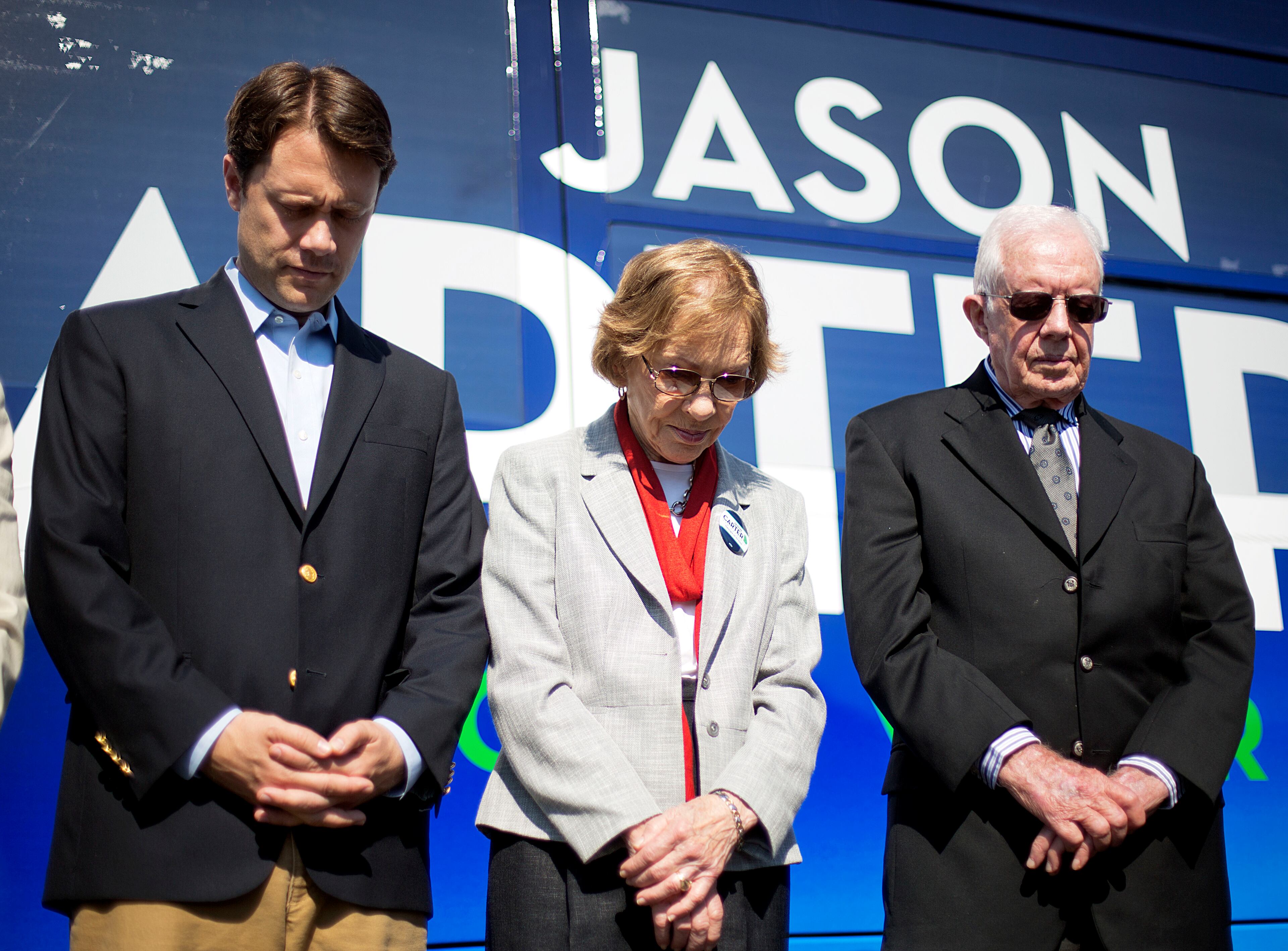Georgia Democratic gubernatorial candidate Jason Carter, left, bows his head during a moment of prayer while standing on stage during a campaign stop with grandfather, former President Jimmy Carter, right, and former first lady Rosalynn Carter, Monday, Oct. 27, 2014, in Columbus, Ga. (AP Photo/David Goldman)