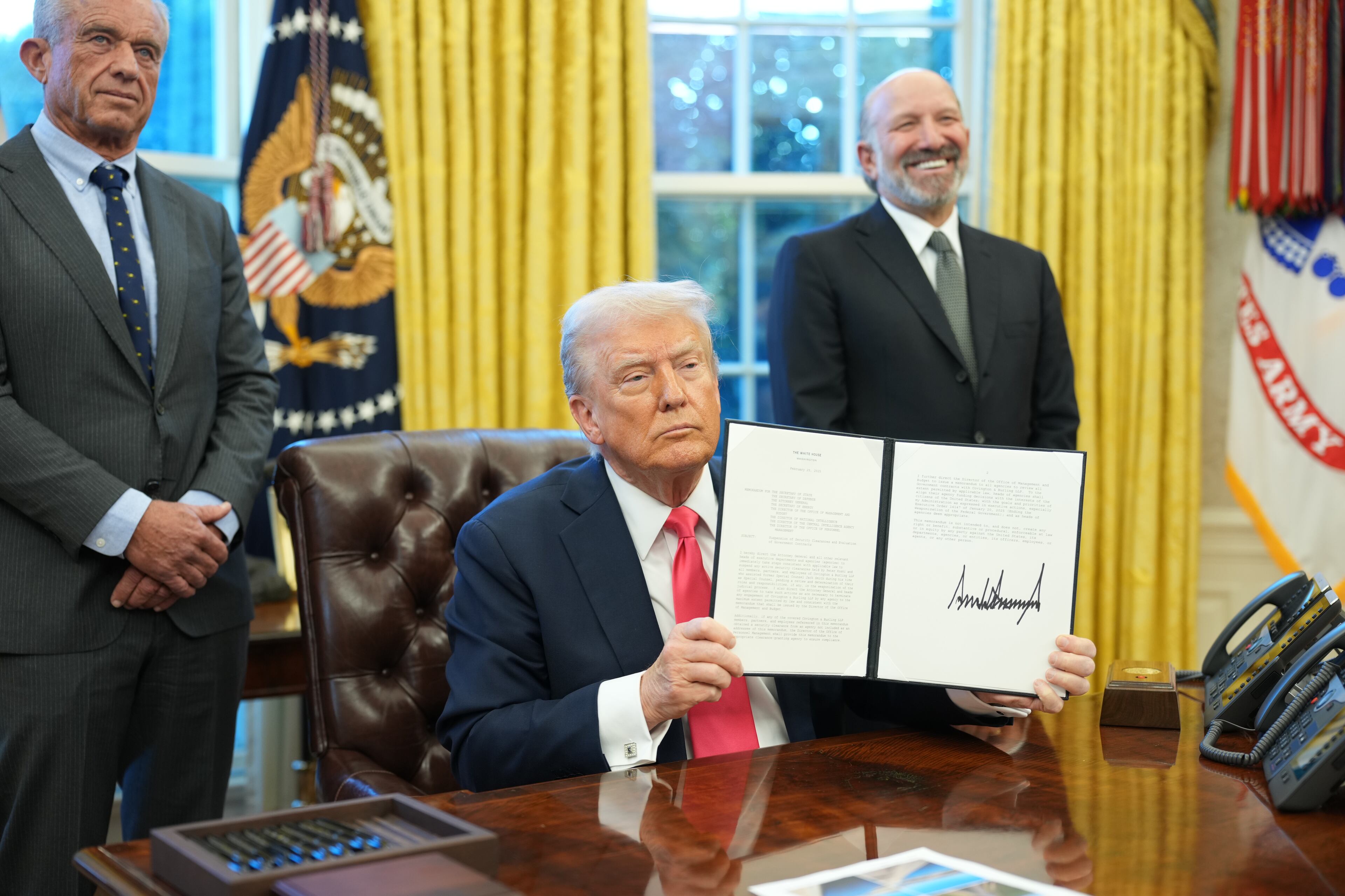 FILE — President Donald Trump holds up an executive order after signing it in the Oval Office of the White House in Washington, on Tuesday, Feb. 25, 2025, as Secretary of Health and Human Services Robert F. Kennedy Jr., left, and Commerce Secretary Howard Lutnick look on. A specious theory on pardons had help from the conservative Heritage Foundation before President Trump and right-wing influencers amplified it. (Doug Mills/The New York Times)