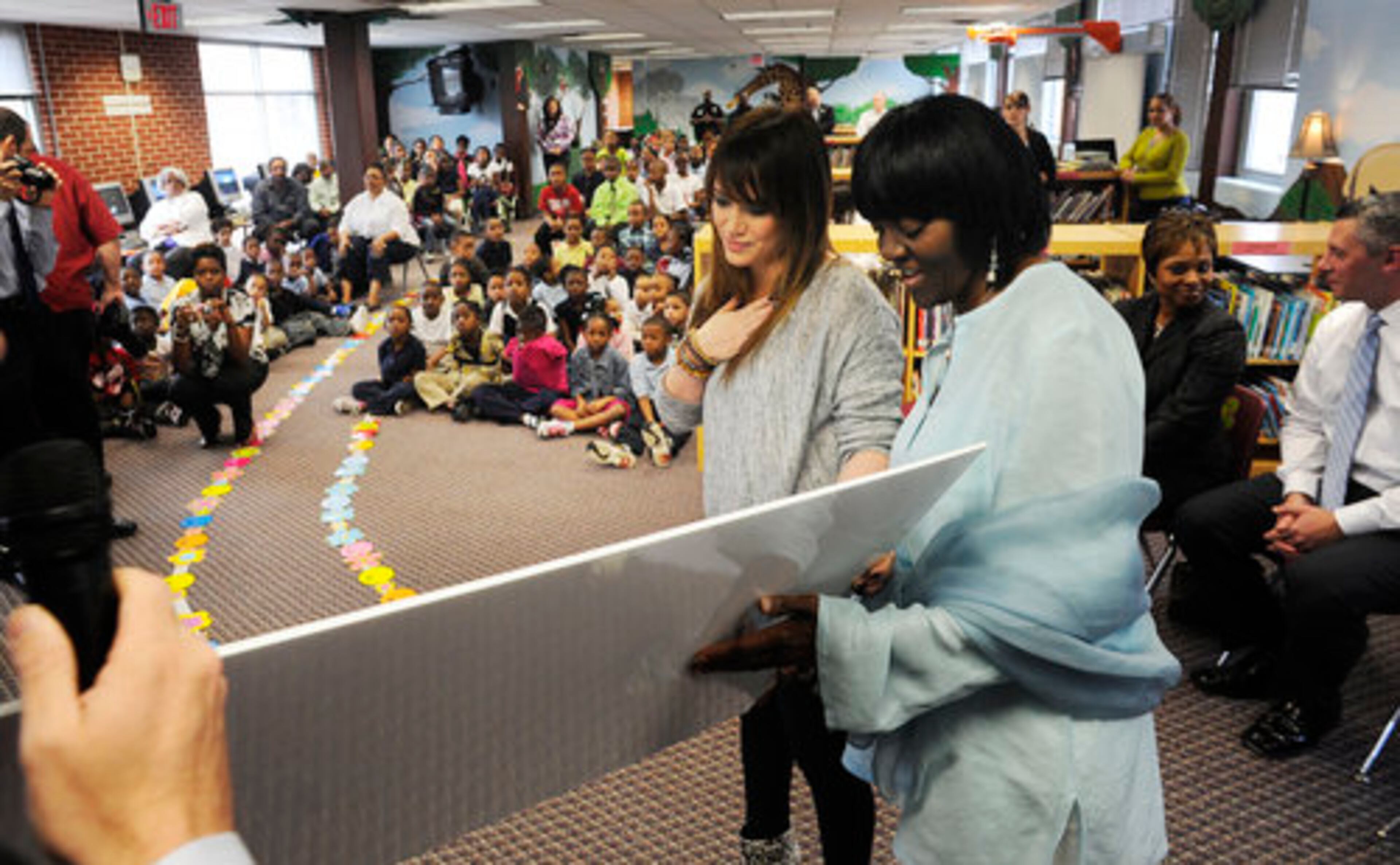 Hilary Duff reacts while a check she is holding with Principle RoseMary Hamer, right, is revealed during a visit to Bethune Elementary School in support of the "Blessings in a Backpack" program, Monday, March 21, 2011. The program picks up where the public school "Free/Reduced Price Meal" program leaves off by feeding children on the weekend with meals loaded into backpacks, a time when those federally funded meals aren't available.