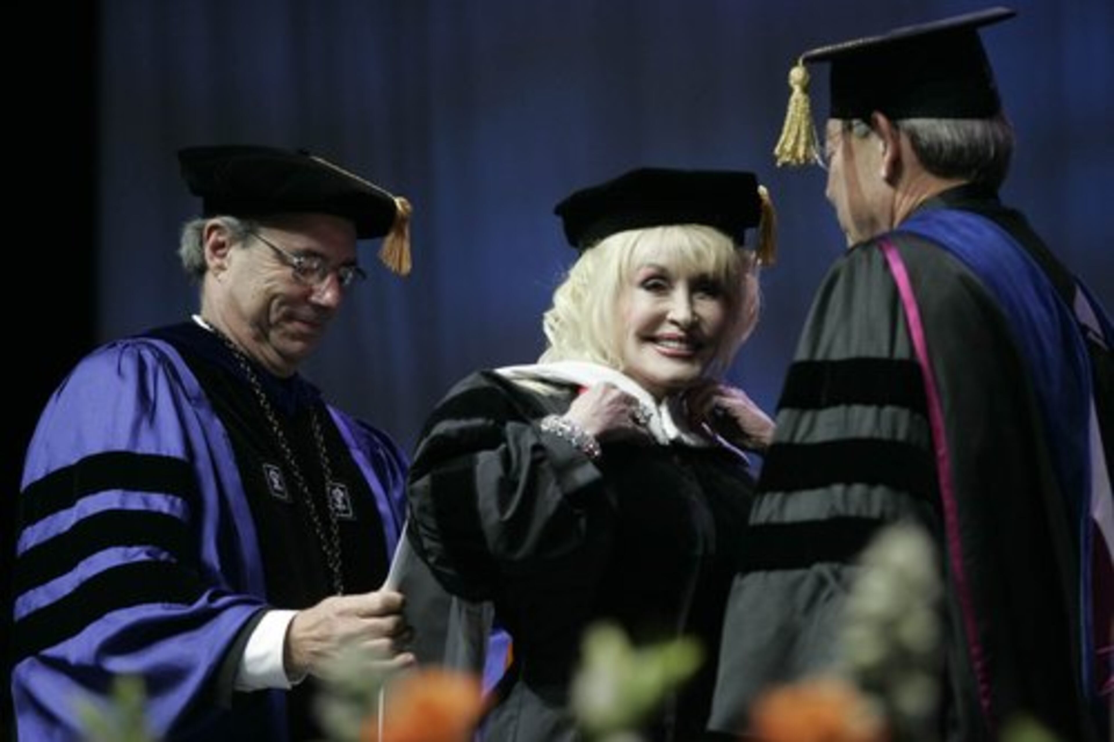 Dolly Parton receives an honorary doctorate of humane and musical letters from the Univerity of Tennessee. Helping her with her robe is acting President Jan Simek (left) and Chancellor Jimmy Cheek.